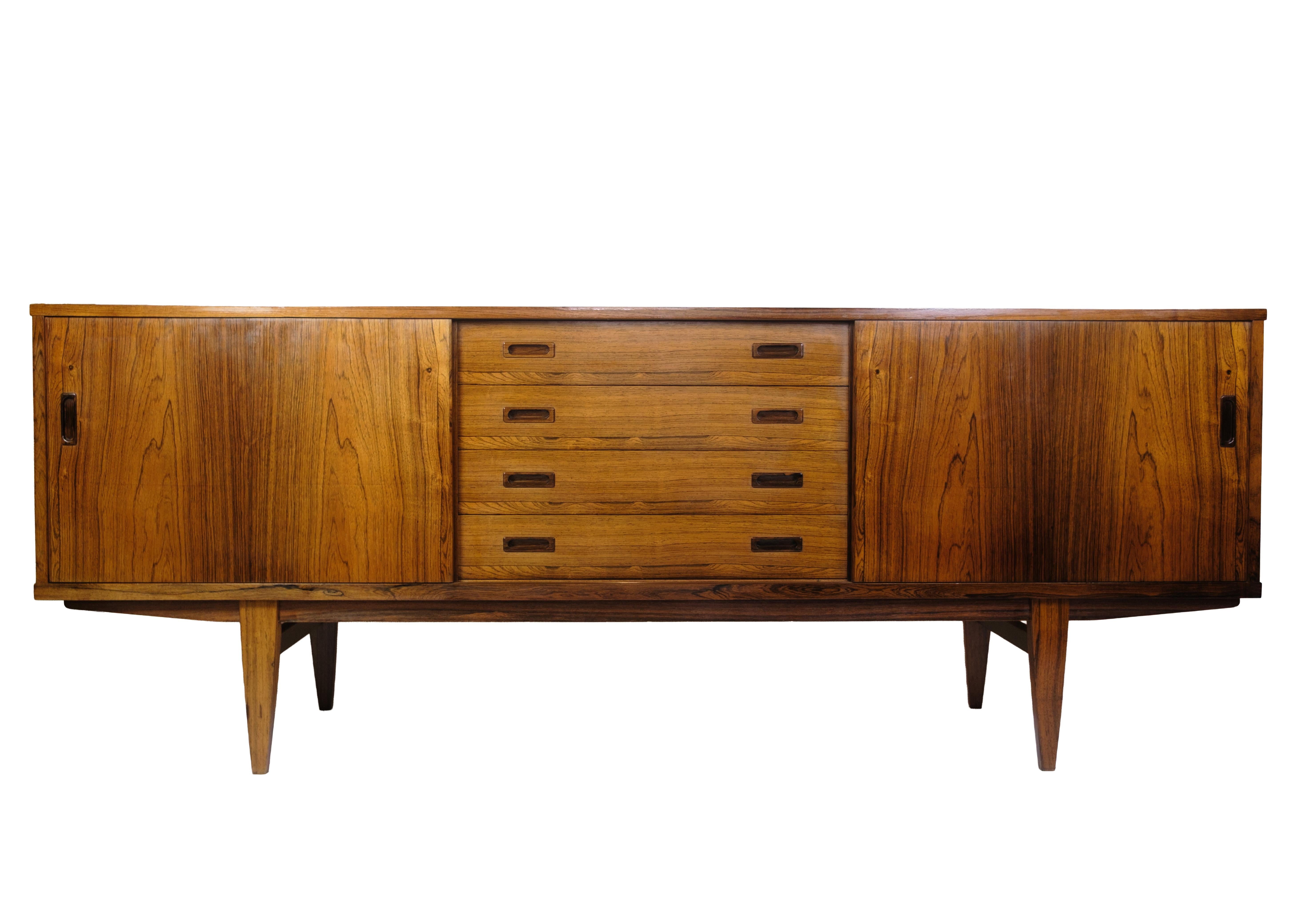 Large sideboard in rosewood with distinctive grain patterns, sliding doors and four centrally placed drawers with milled handles. The complete design and the slightly sloping legs give the furniture a floating lightness that characterizes Danish