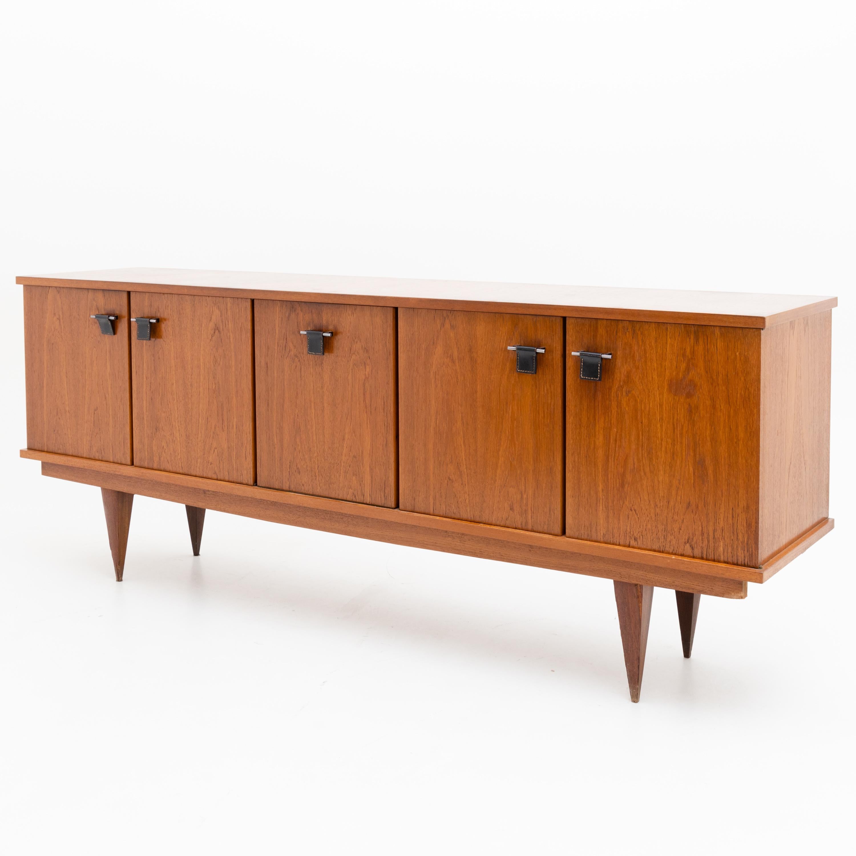 Large sideboard on square tapered feet with five doors and metal handles with brown leather pulls. Labels on the inside.