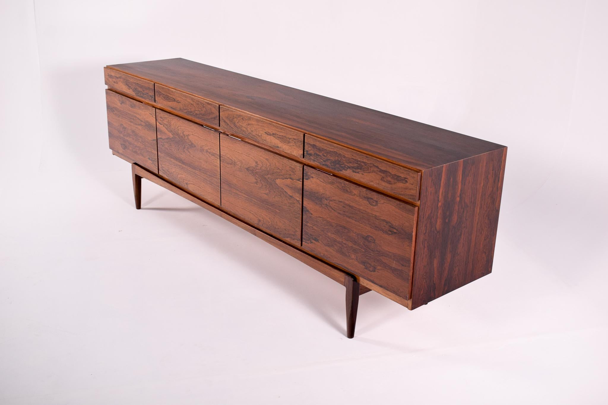 Designed by Ib Kofod-Larsen and manufactured in Denmark in the 1960s, this clean-lined sideboard features beautifully rosewood. The case sits on a raised base and offers four drawers above a four-door cabinet.