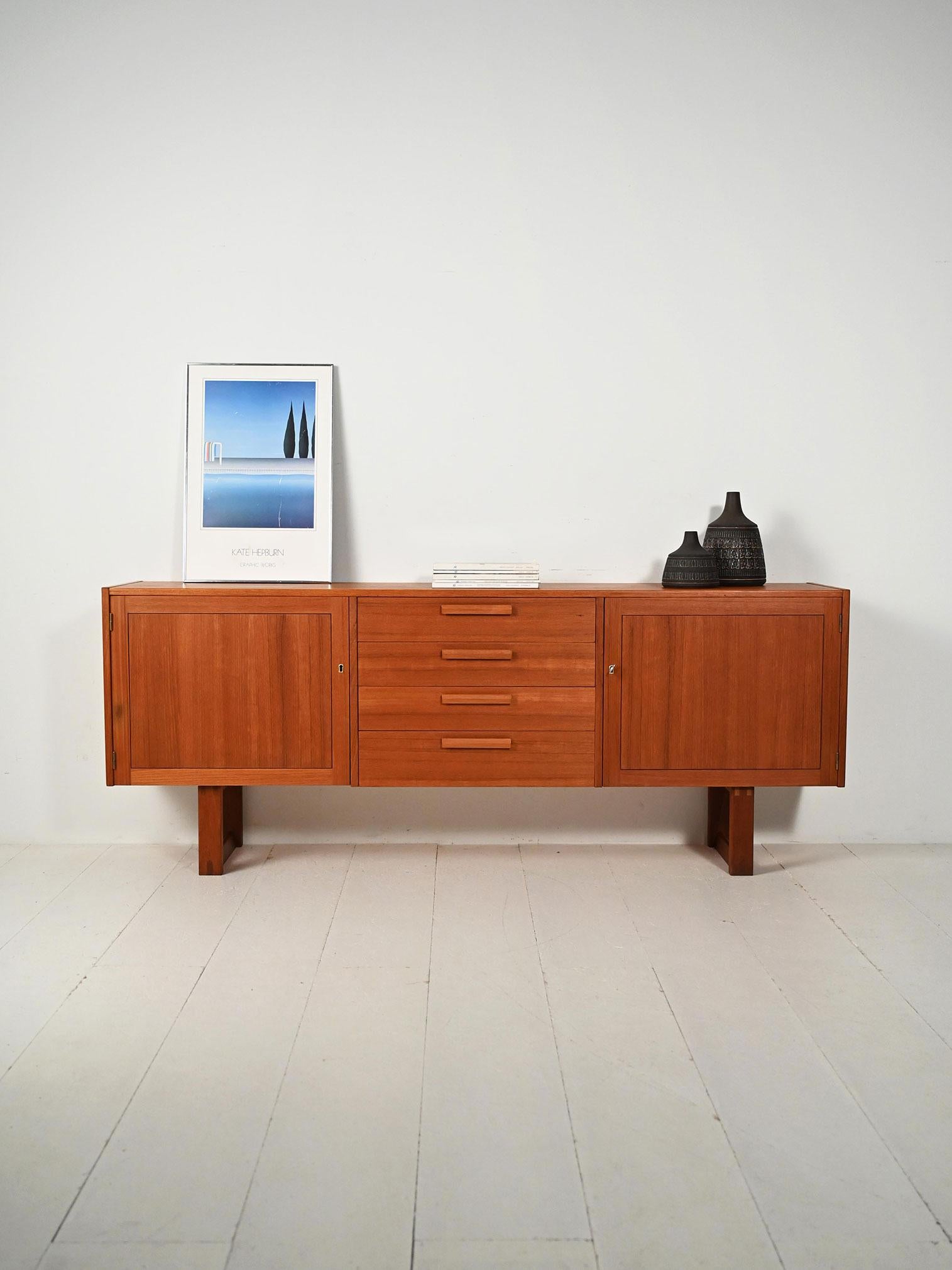 Sideboard Domi Monté di Nils Jonsson per Troeds in teak con due vani e cassetti centrali.

Buffet modèle Domi Monté de Nils Jonsson pour Troeds, réalisé en teck avec des veines disposées dans diverses orientations. Due vani con mensole dietro ante a
