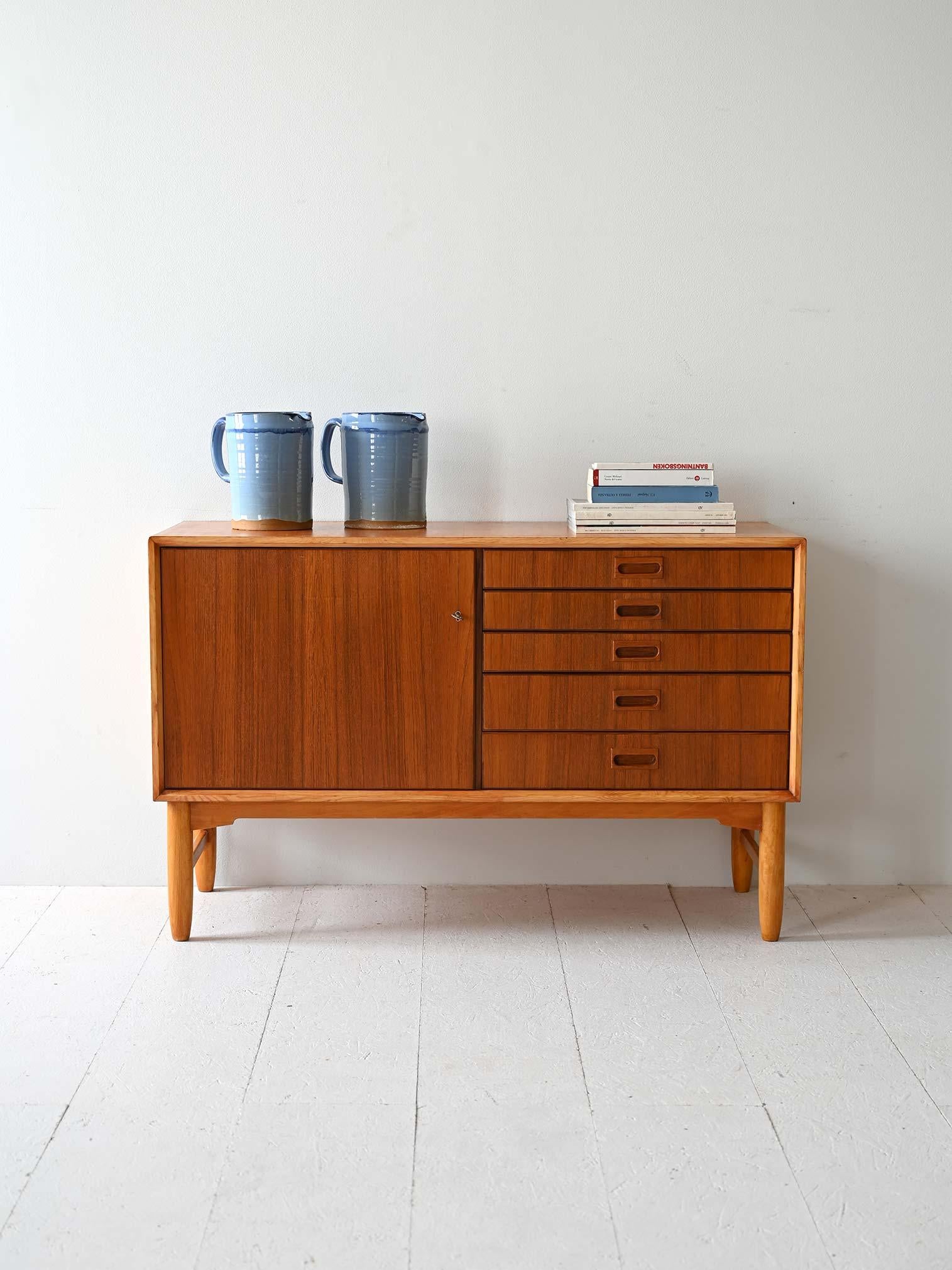 Buffet vintage en teck avec pieds et profils en chêne. Équipé d'une porte à charnières et de cinq tiroirs.

Le buffet est doté d'une porte à charnières qui dissimule un grand espace fonctionnel, à côté duquel les cinq tiroirs alignés verticalement