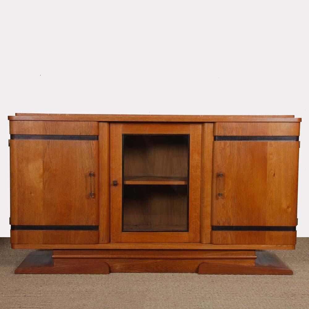 This oak enfilade dates from the 1950s. It opens with two doors on each side, with glass handles. In the center is a lockable display cabinet. This sideboard is in good original condition. The top has been restored.
