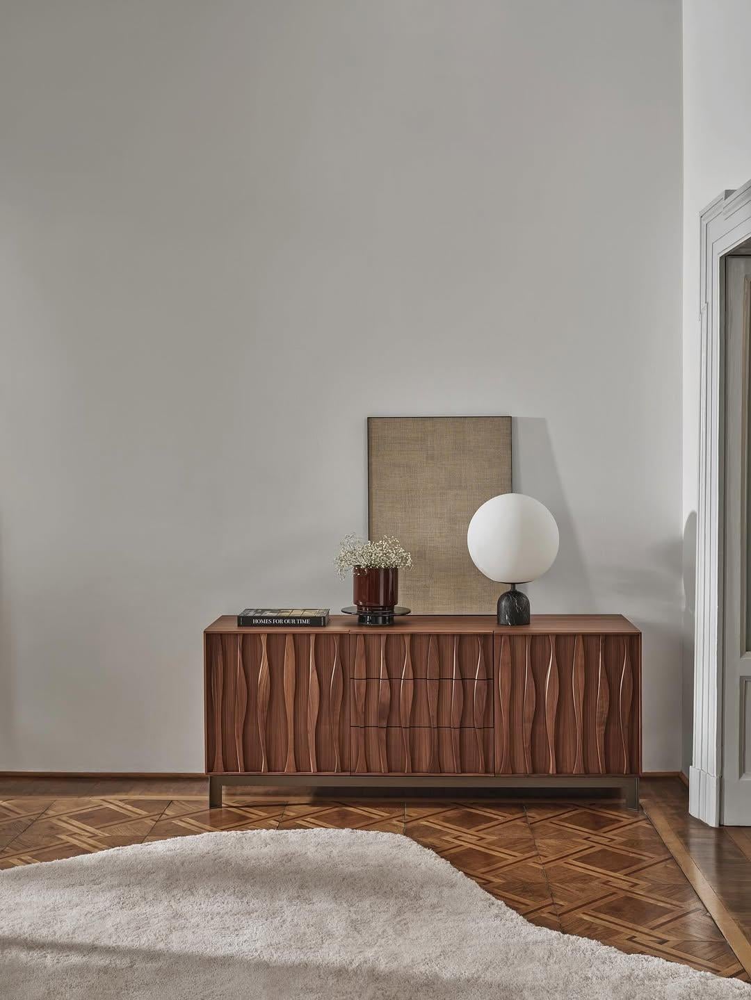 Brand: Porada
Design: Marconato & Zappa
Model: Masai Sideboard

The Masai Sideboard by Porada, designed by Marconato & Zappa, features a striking wave decoration carved in solid Canaletto walnut inserts across its front. This refined piece of