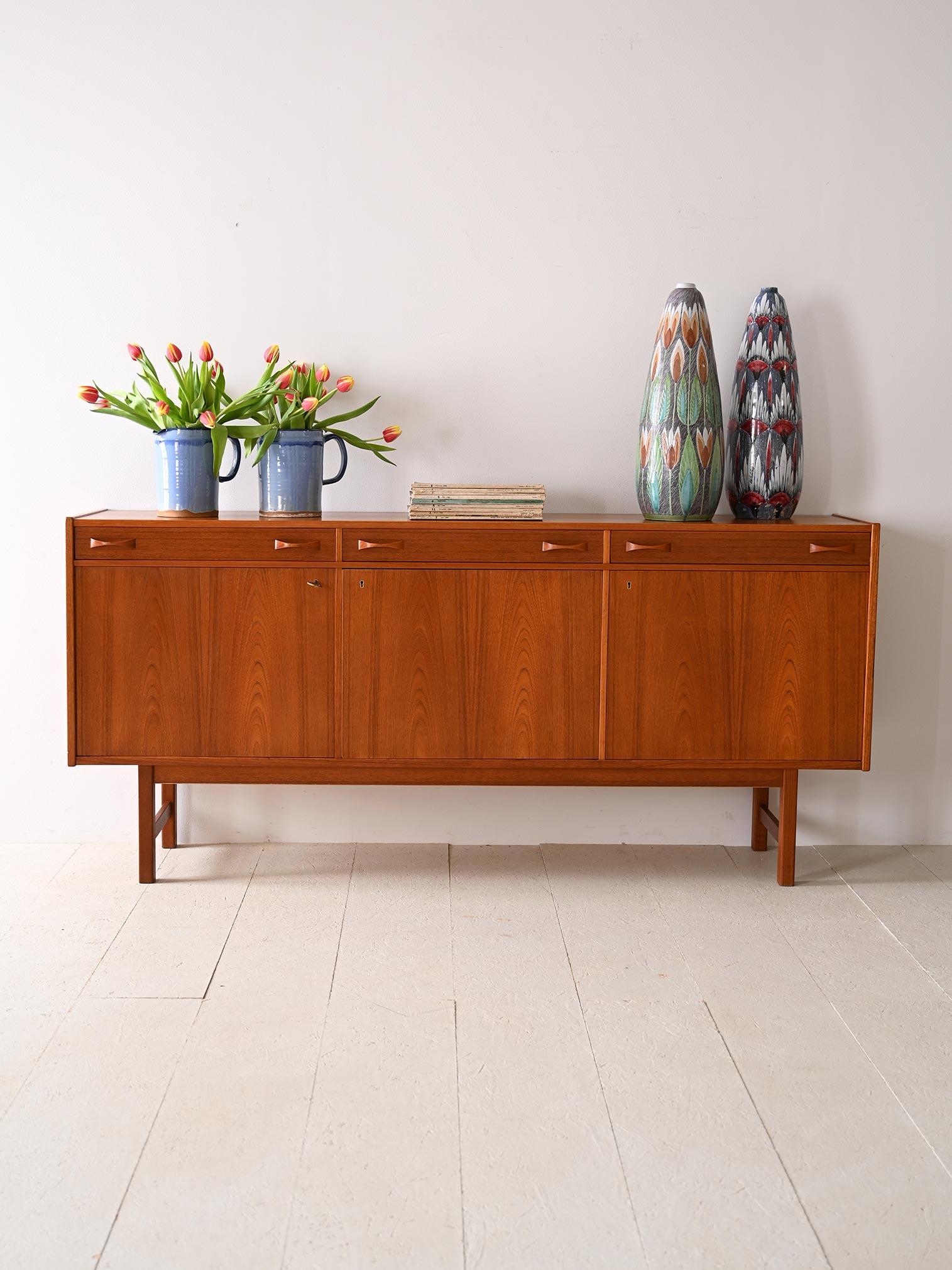 Vintage teak sideboard with doors and drawers.

A design icon characterized by clean, square lines that lend a modern touch to any room. Crafted from fine teak wood in warm, enveloping tones, this piece embodies the quintessential Nordic
