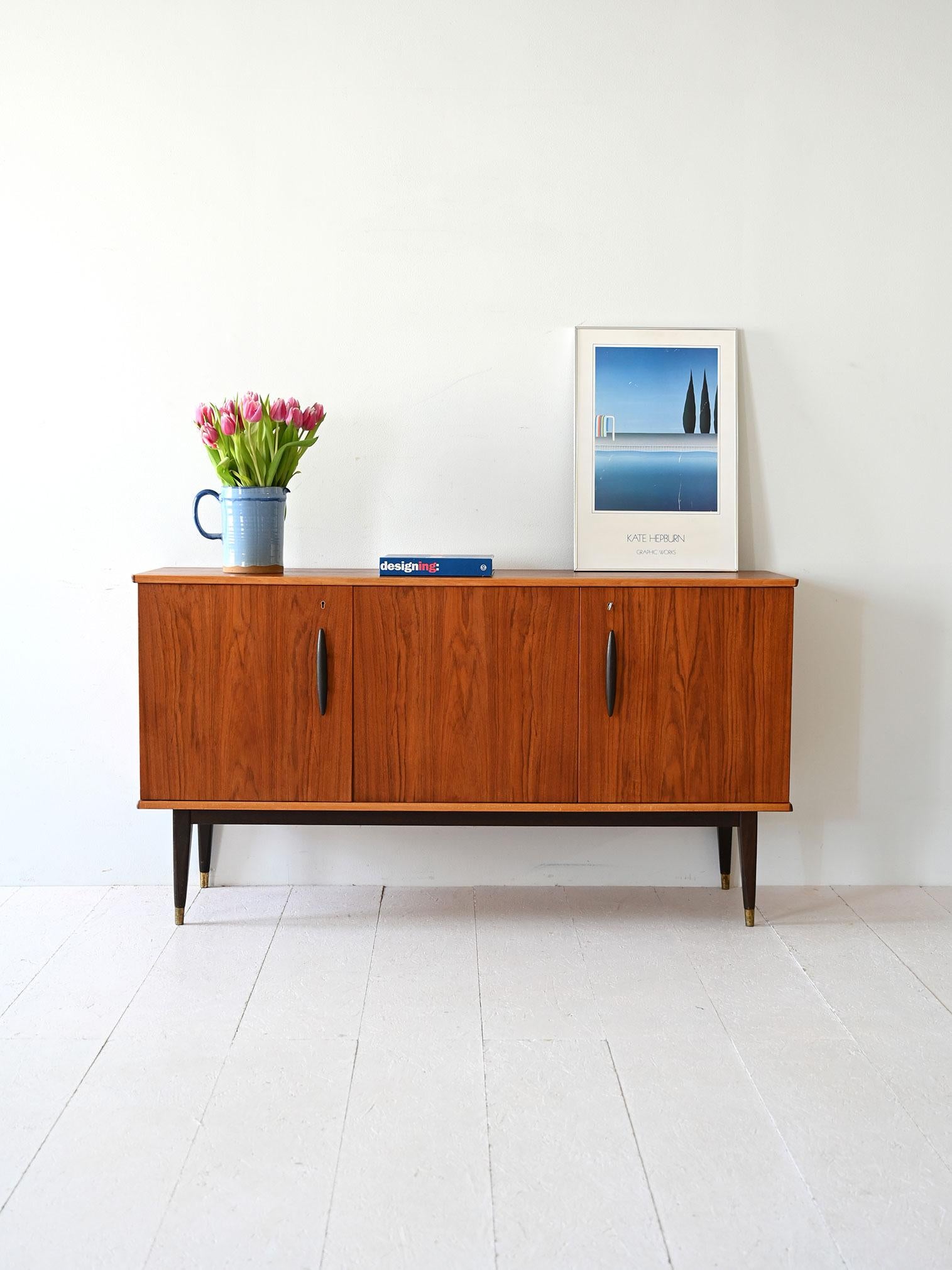 Teak sideboard with hinged doors, three interior compartments, feet with metal details and contrasting handles.

Scandinavian sideboard from the 1950s, made of teak with an essential design and refined details. The frame consists of three hinged