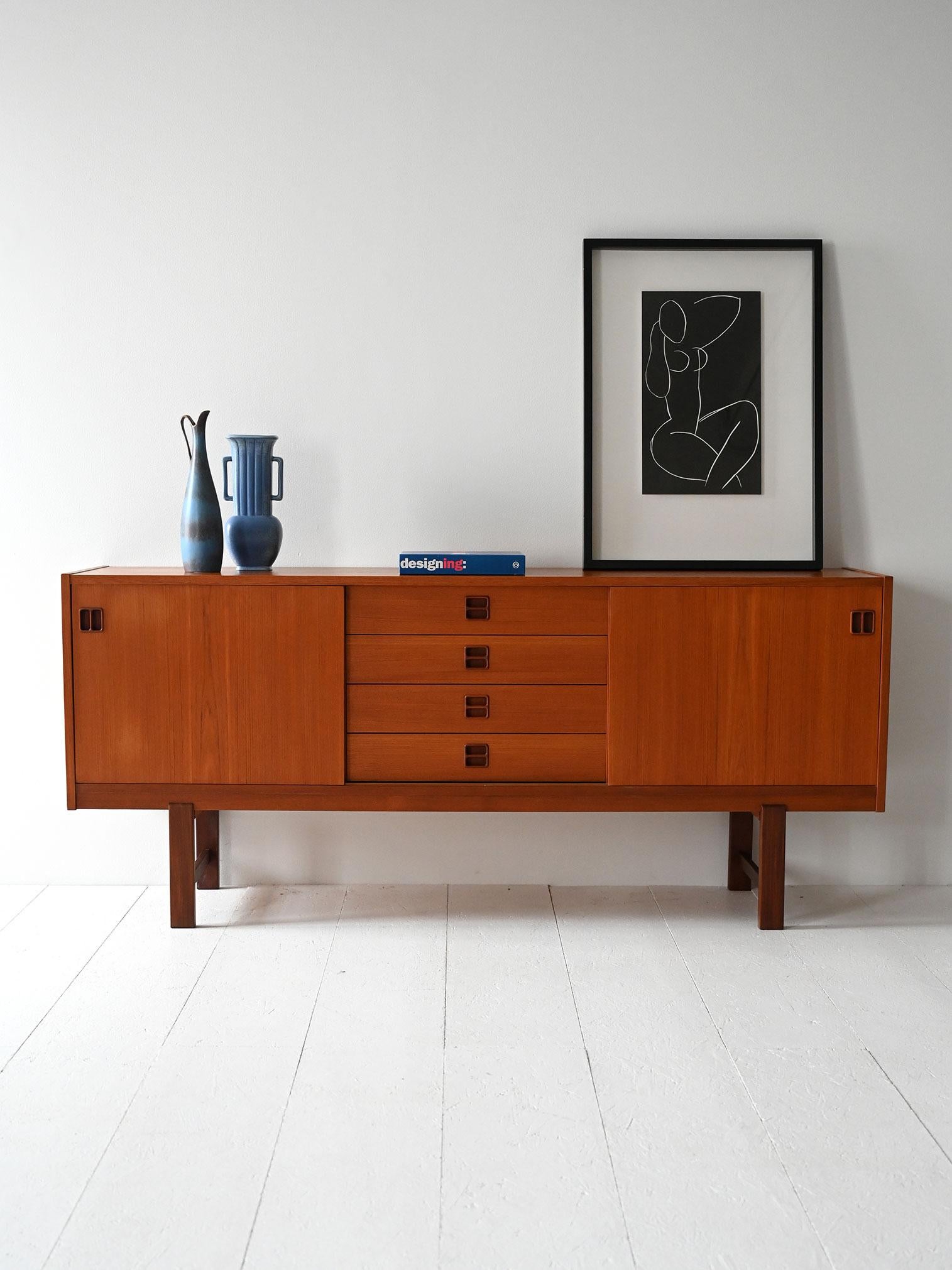 Teak sideboard with sliding doors, center drawers and square feet in contrasting darker wood.

Scandinavian 1960s teak sideboard, featuring a clean structure with two sliding side doors and four central drawers. Recessed handles and dark wood square