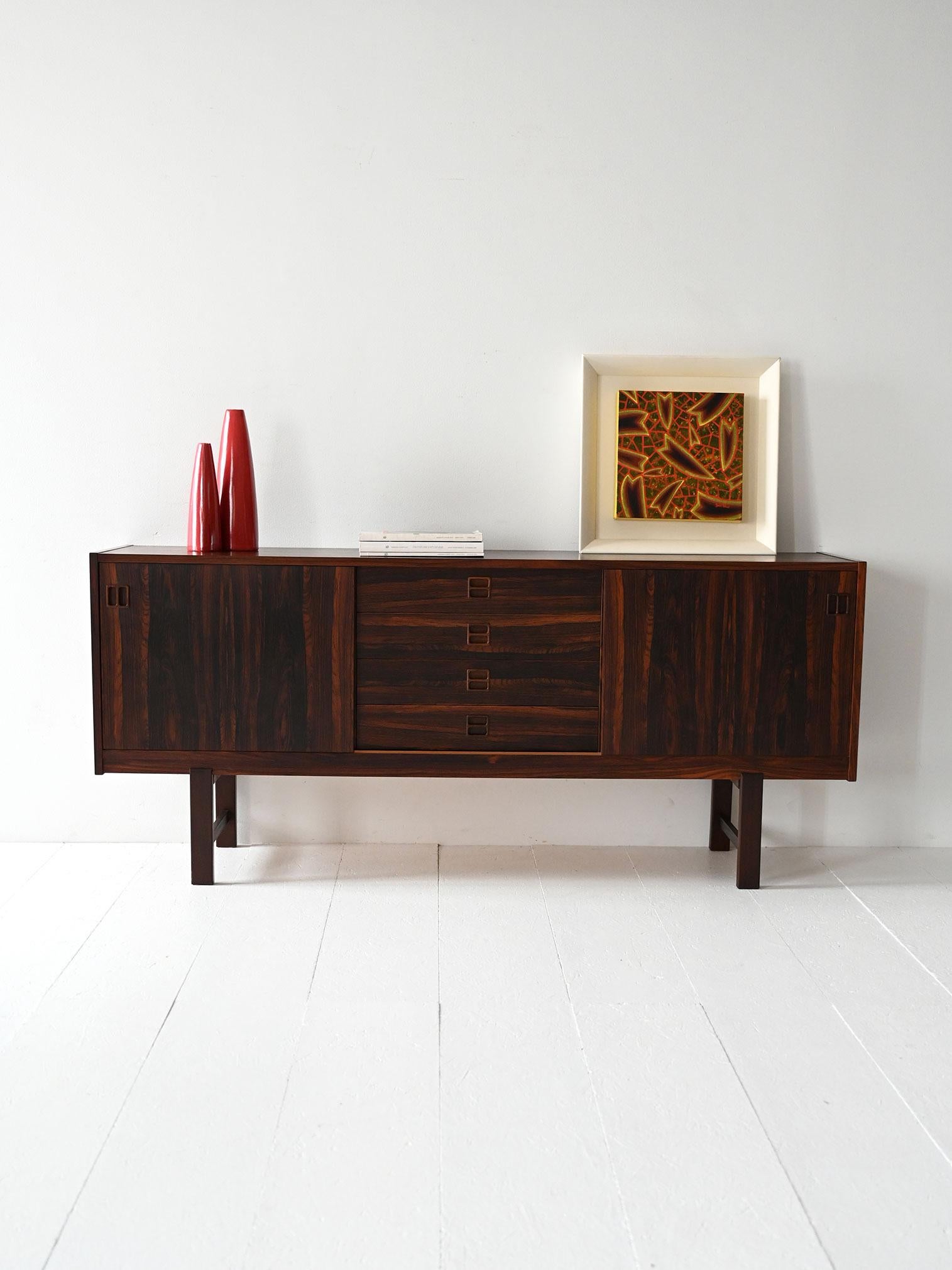Rosewood sideboard with marked grain, central drawers and sliding doors. Rectangular legs with an elegant profile.

Vintage 1960s Scandinavian sideboard in rosewood with an intense, regular grain. The cabinet features a central block of four drawers