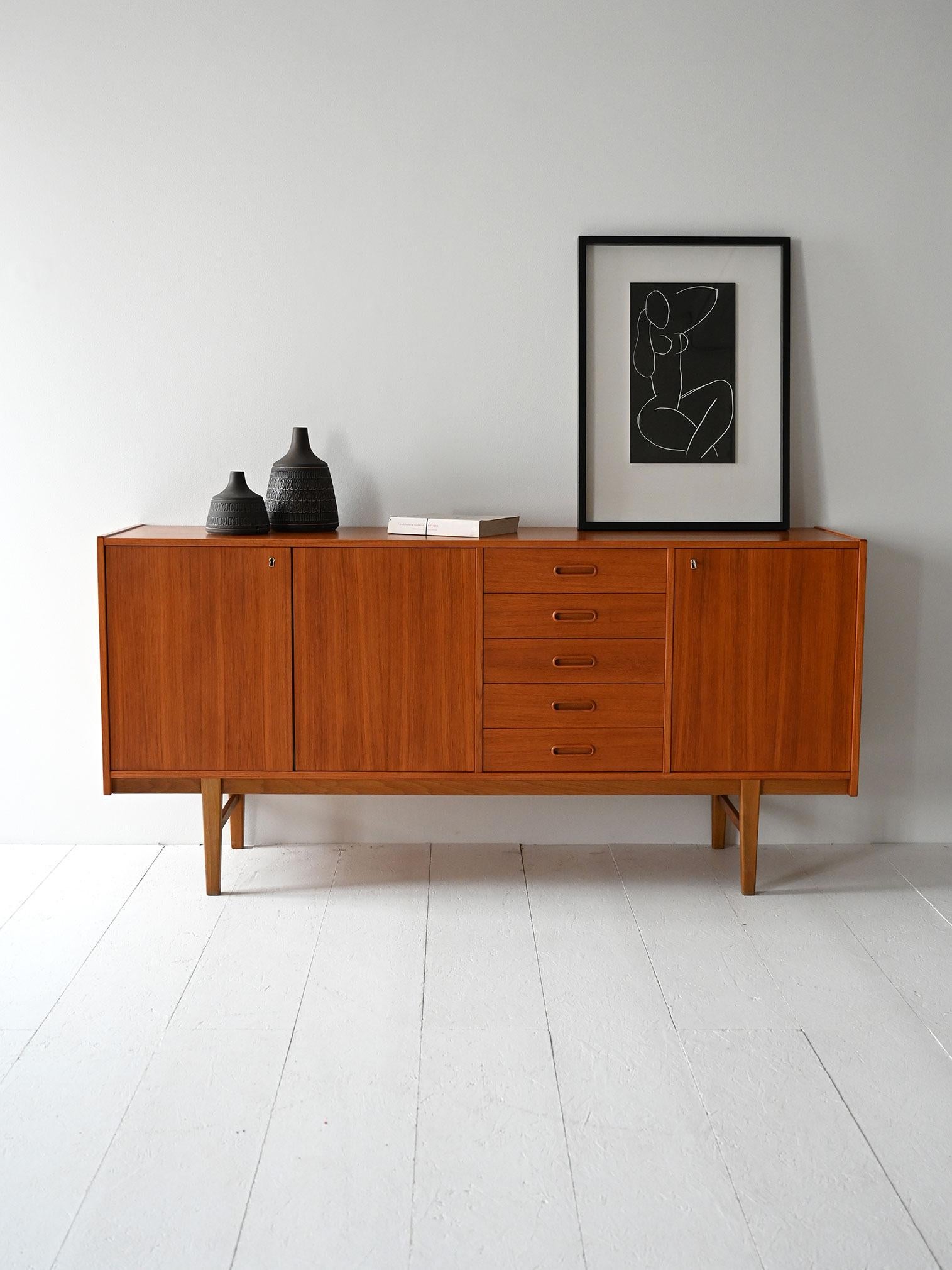 Vintage 1960s Scandinavian sideboard with teak frame, hinged doors and center drawers, raised on geometric feet.

Essential design and balanced proportions for this Scandinavian teak sideboard made in the 1960s. Two hinged doors on the left side,