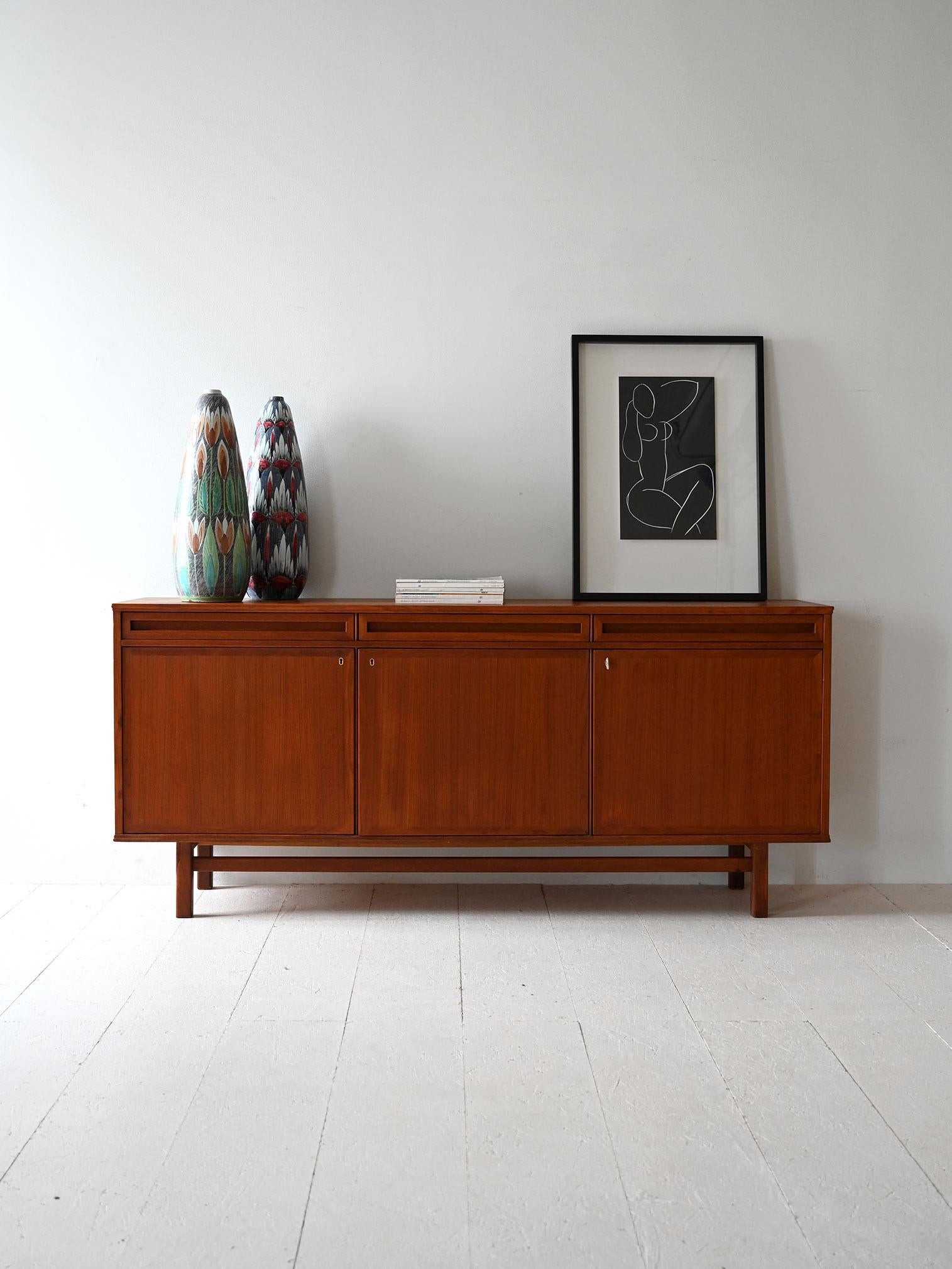 1950s/60s teak sideboard, three hinged doors, three top drawers.

Vintage Scandinavian sideboard from the 1950s/60s made of teak with an understated and rigorous design. The structure develops into three hinged doors at the bottom and three top