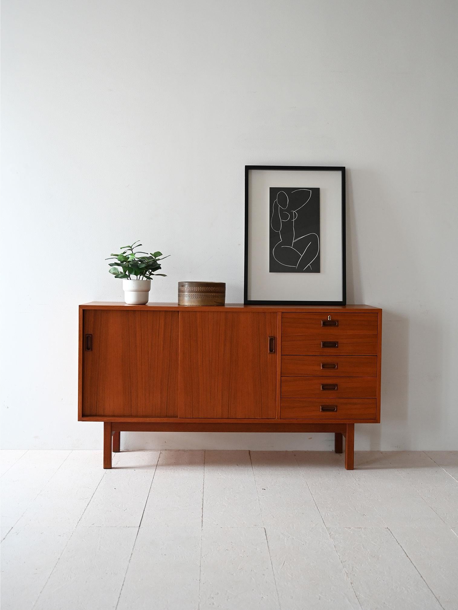 Sideboard vintage con struttura in teak anni ’60, ante scorrevoli, quattro cassetti e maniglie intagliate a contrasto.

Sideboard scandinavo vintage degli anni ’60 realizzato in teak. Le ante scorrevoli a filo rivelano un vano con mensola interna,