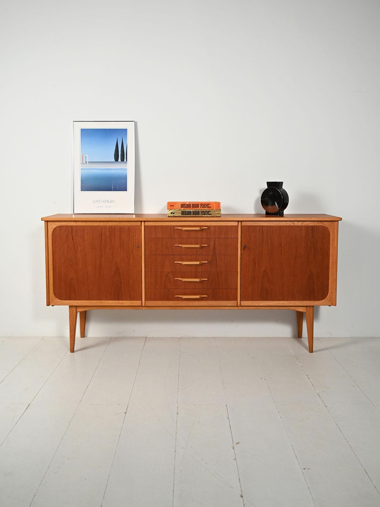 Sideboard scandinavo anni ’50/’60 in teak e rovere, due vani con mensole e cassetti centrali con maniglie scolpite in rovere.

Struttura in teak con cornici arrotondate e top leggermente sporgente definisce il sideboard anni ’50/’60. Le ante