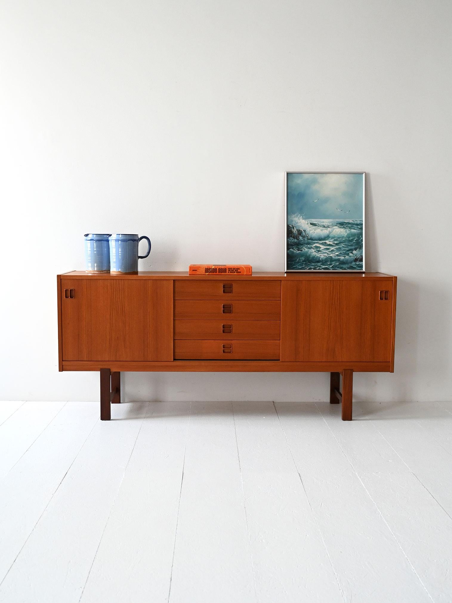 Vintage teak sideboard with sliding doors, four center drawers and contrasting dark legs.

Scandinavian sideboard from the mid-1960s, in teak with contrasting dark legs. Two side sliding doors flank a central row of four drawers. The recessed,
