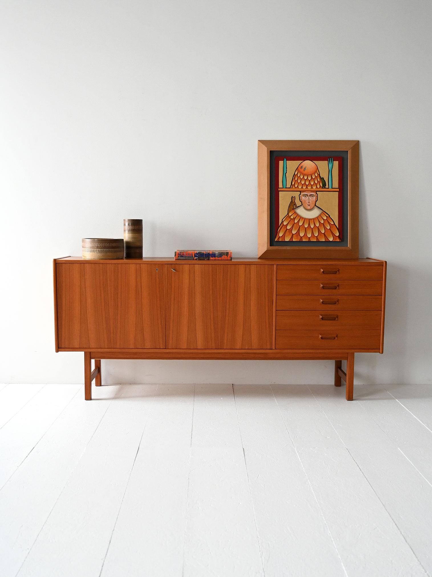 Vintage teak sideboard with hinged doors, side drawers, and original cutlery divider.

Scandinavian sideboard from the 1950s/60s made of teak, with two hinged doors and interior shelf. The vertically arranged side drawers feature carved handles; the