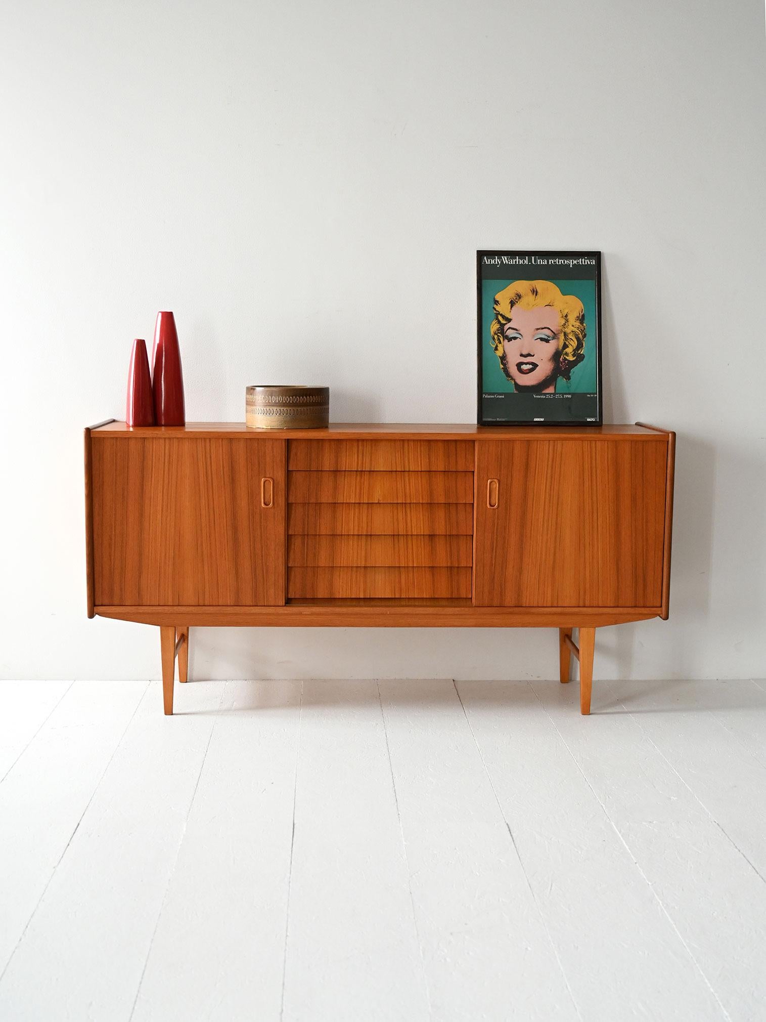 Credenza anni ’50/’60 in teak con cassetti centrali a tegola e due ante scorrevoli laterali.

Sideboard scandinavo anni ’50/’60 in teak con struttura leggera e gambe rastremate. Al centro, sei cassetti a tegola; ai lati, due vani con ante scorrevoli