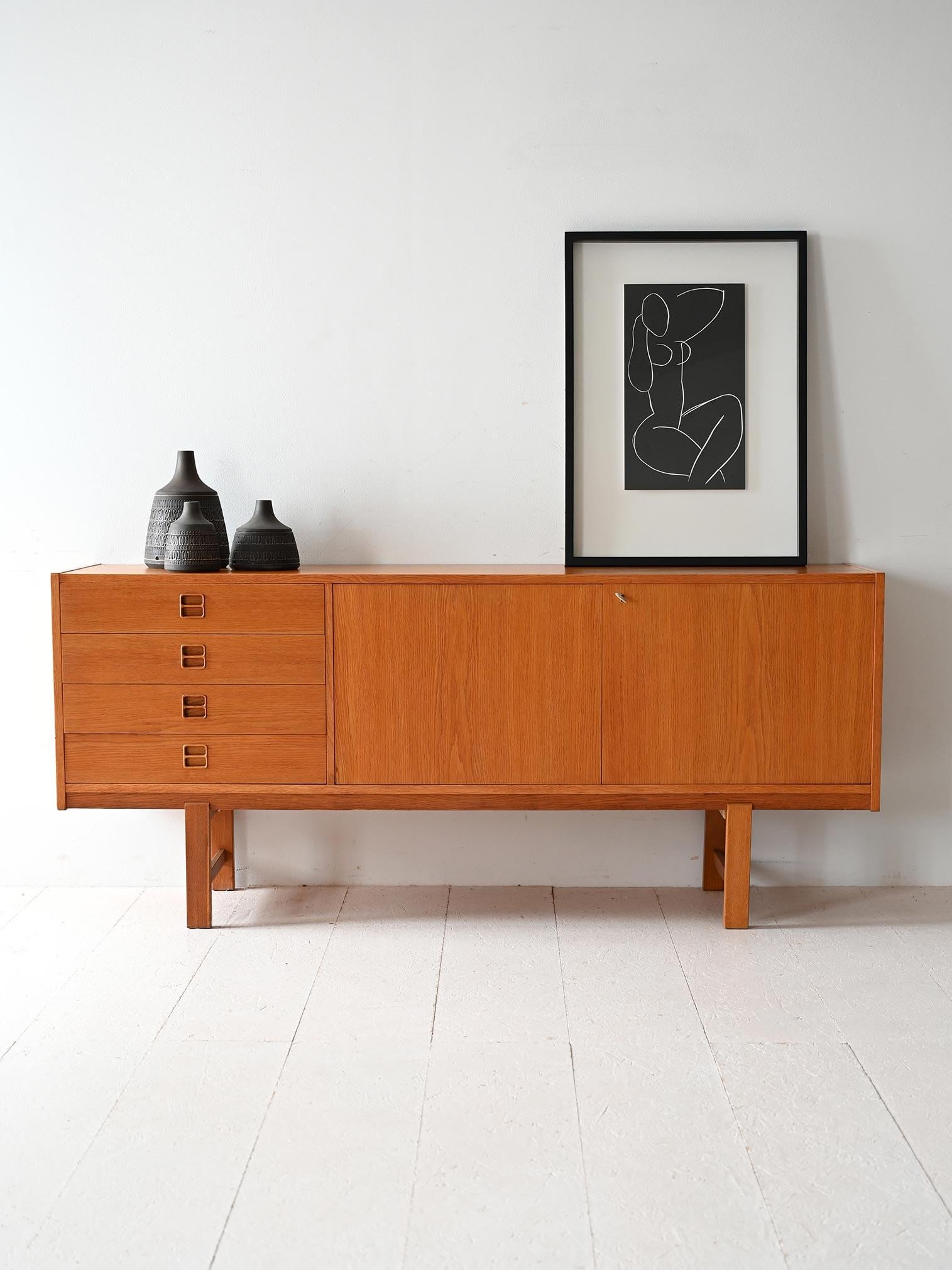 Sideboard scandinavo degli anni '60 in rovere con quattro cassetti, ante a battente e vano con mensola interna.

Sideboard scandinavo vintage realizzato in rovere, con una struttura solida ed essenziale. A sinistra, quattro cassetti con maniglie