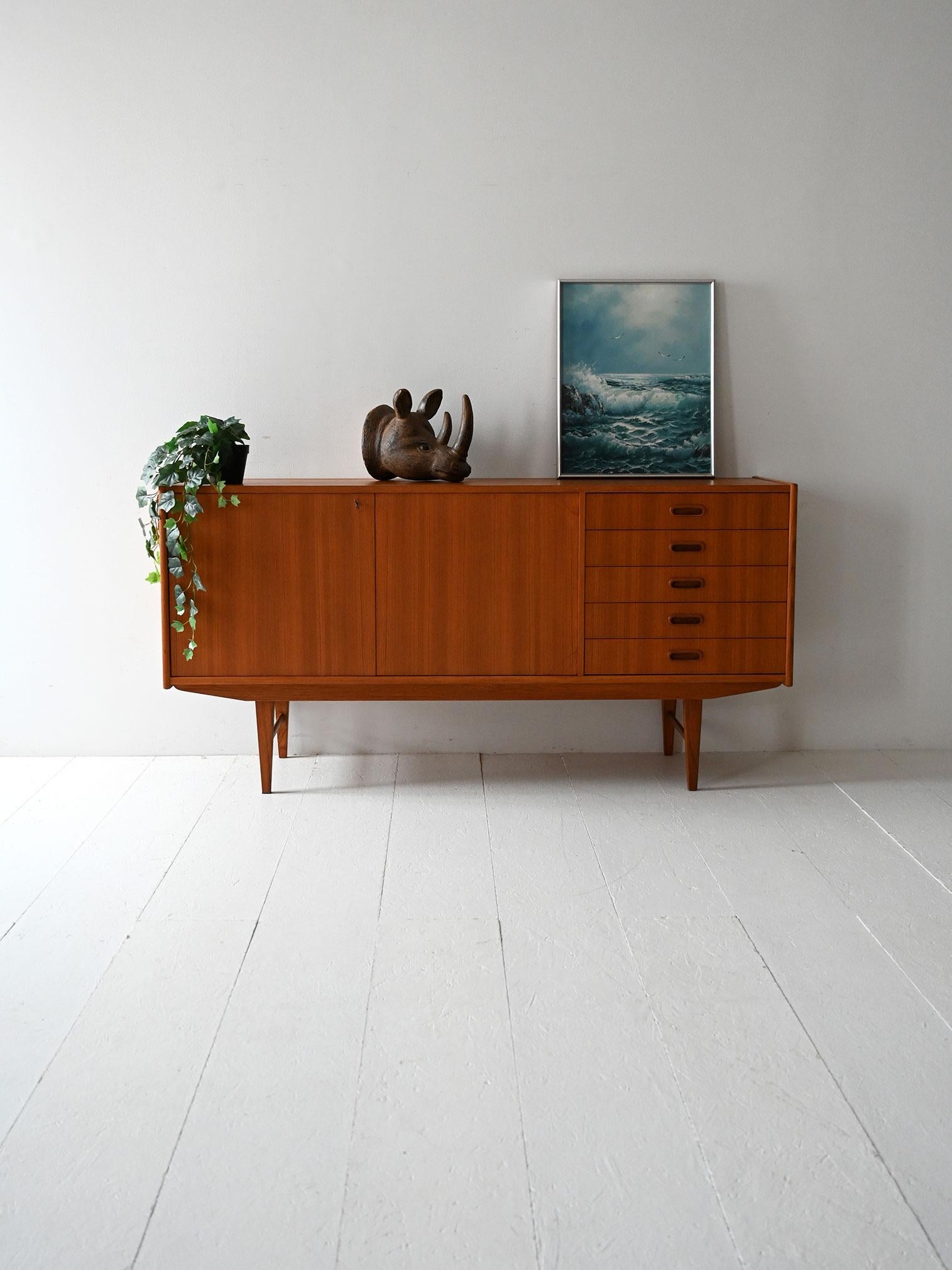 Sideboard scandinavo vintage in teak anni ’60 con due ante, cinque cassetti e gambe rastremate dal profilo ortogonale.

Sideboard scandinavo vintage in teak, realizzato negli anni ’60, caratterizzato da linee pulite e proporzioni equilibrate. La