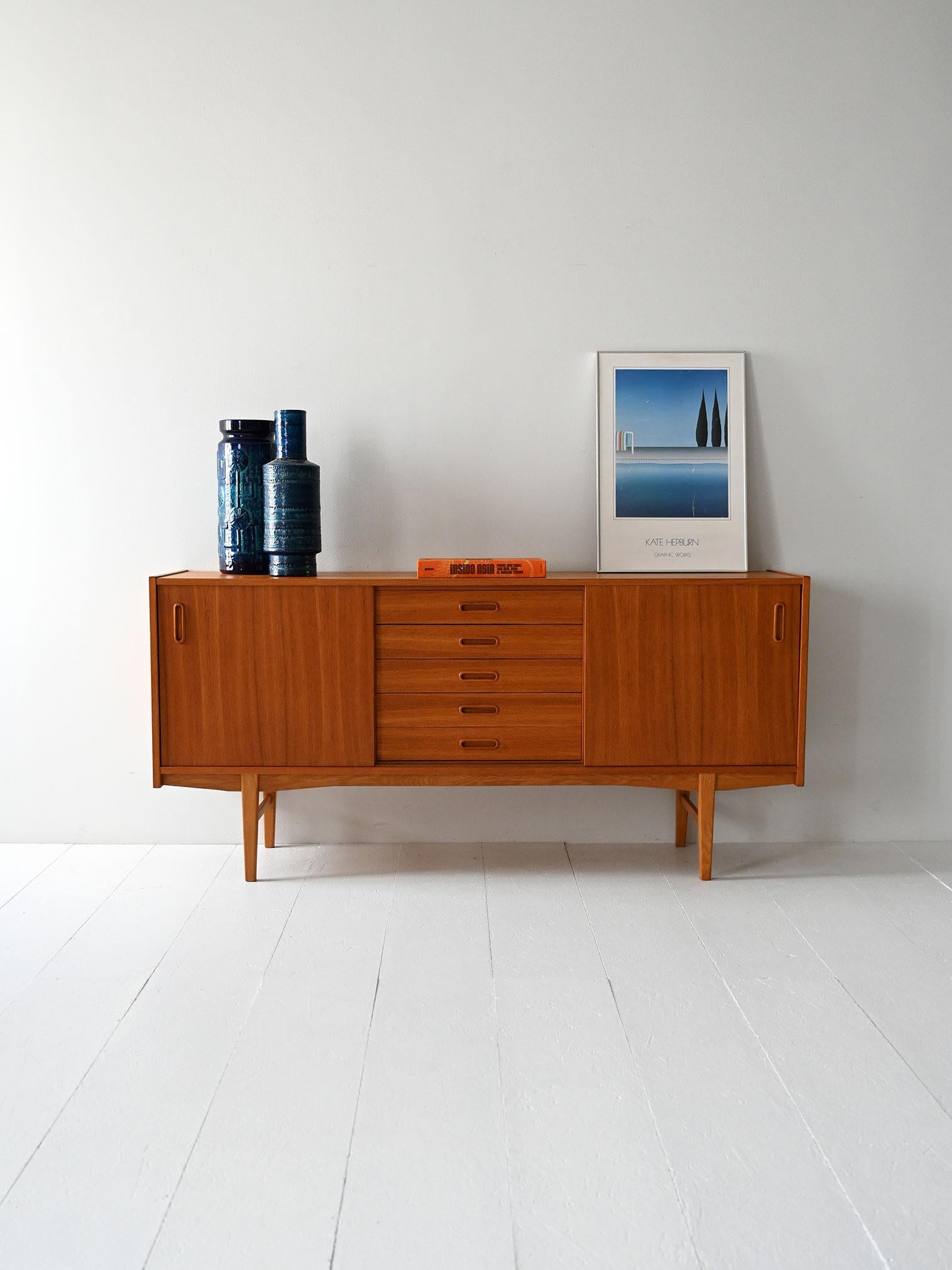 Sideboard with sliding doors and five central drawers, made of teak and oak. Light and functional lines.

Scandinavian 1960s sideboard with teak frame and solid oak legs. Two sliding doors conceal compartments with an interior shelf, while the