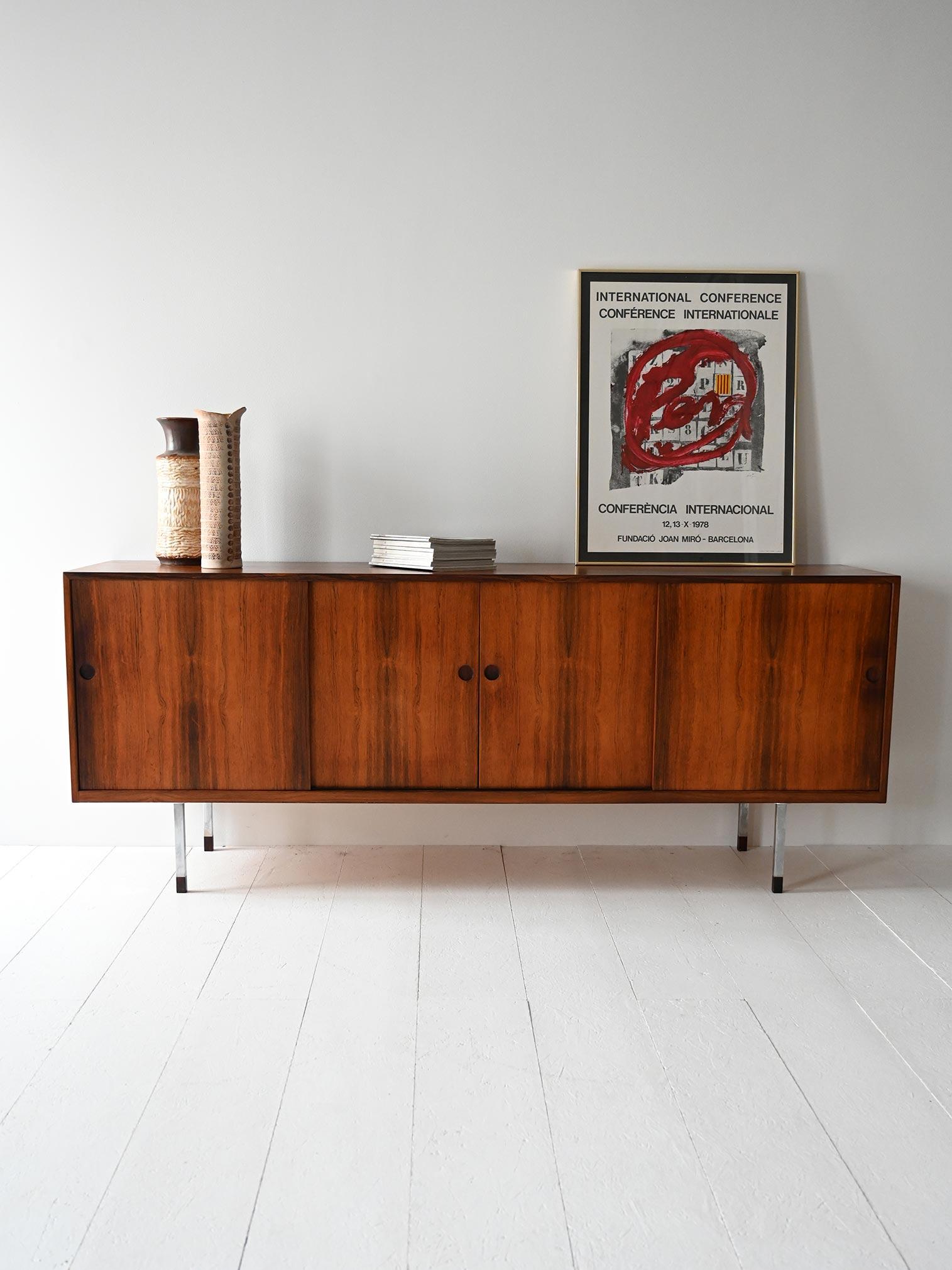 Dänisches Sideboard aus dem Jahr 1961 in Palisander, mit Schiebetüren, Stahlfüßen und eleganten Details.

Skandinavisches Sideboard von Norgaard Mobelfabrik, hergestellt 1961. Er ist aus gemasertem Palisanderholz gefertigt und hat vier Schiebetüren,