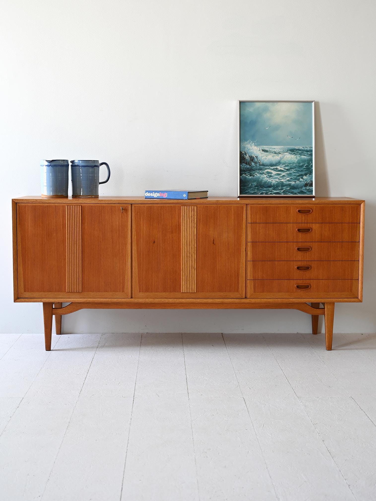 Scandinavian sideboard produced by AB Moblerfabriken in the 1960s. It stands out for the clear profiles and decorations on the light oak doors, which frame and embellish the teak frame.

There are 5 drawers with the handle carved in wood on one side