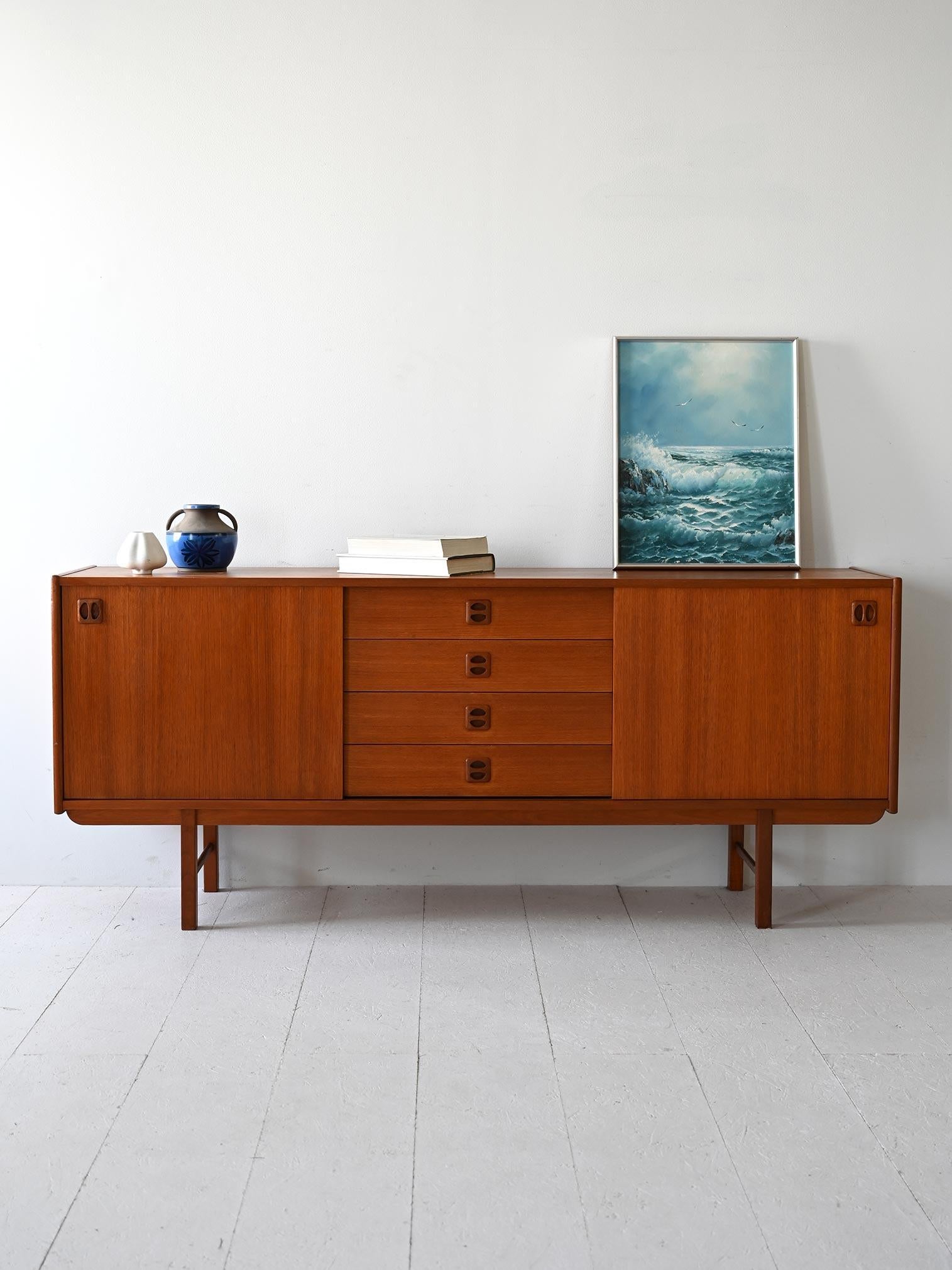Credenza scandinava vintage in teak con cassetti centrali e ante scorrevoli. Le gambe squadrate e le linee minimali la rendono un pezzo moderno e adattao a diversi ambienti. 

Ai lati del mobile si trovano due scompartimenti dotati rispettivamente
