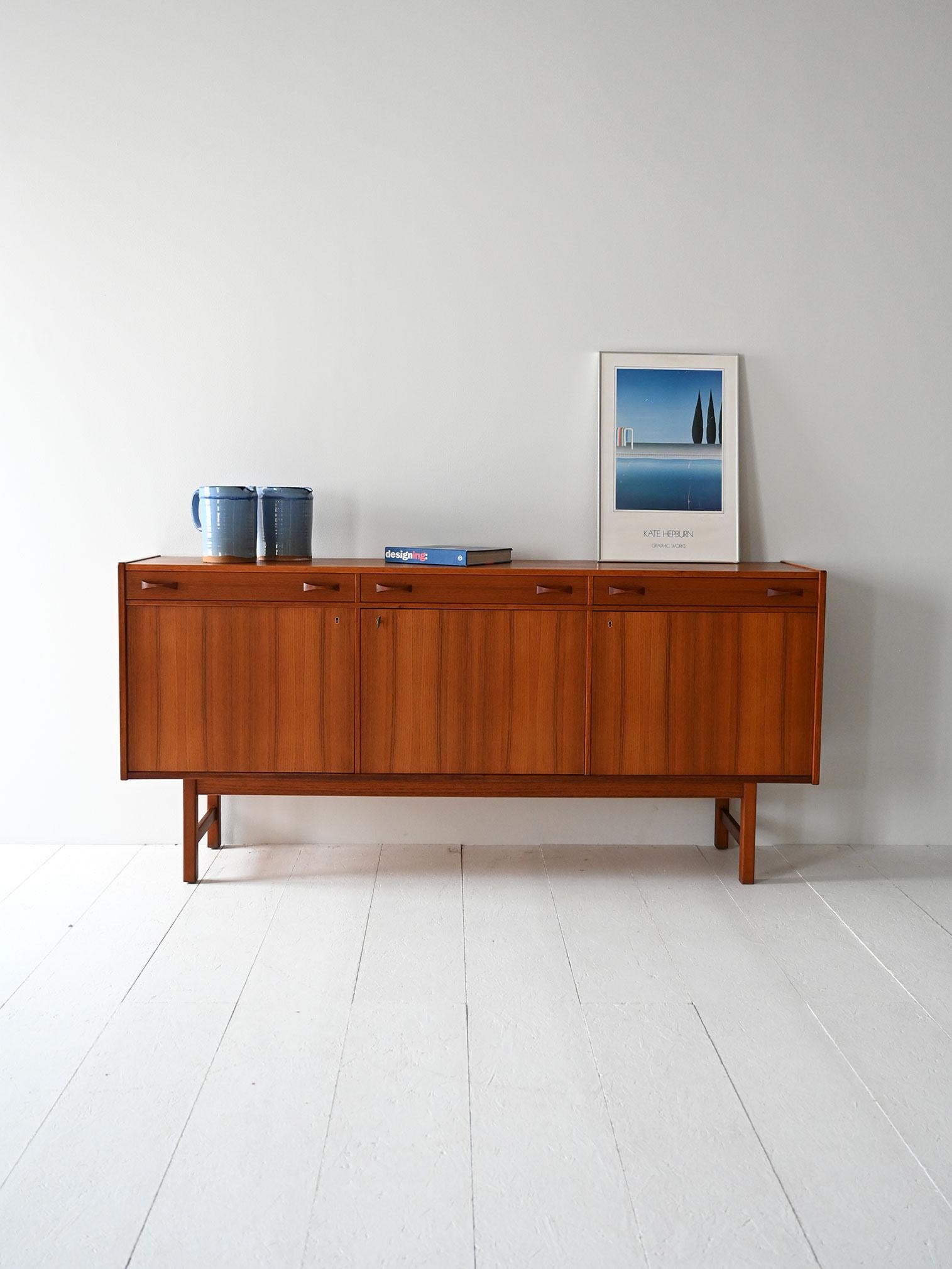 Scandinavian teak sideboard manufactured by Ulferts, with three top drawers, doors below, and original stamp inside.

Manufactured in the 1960s by Ulferts in Sweden, this teak sideboard features a balanced composition with three top drawers and