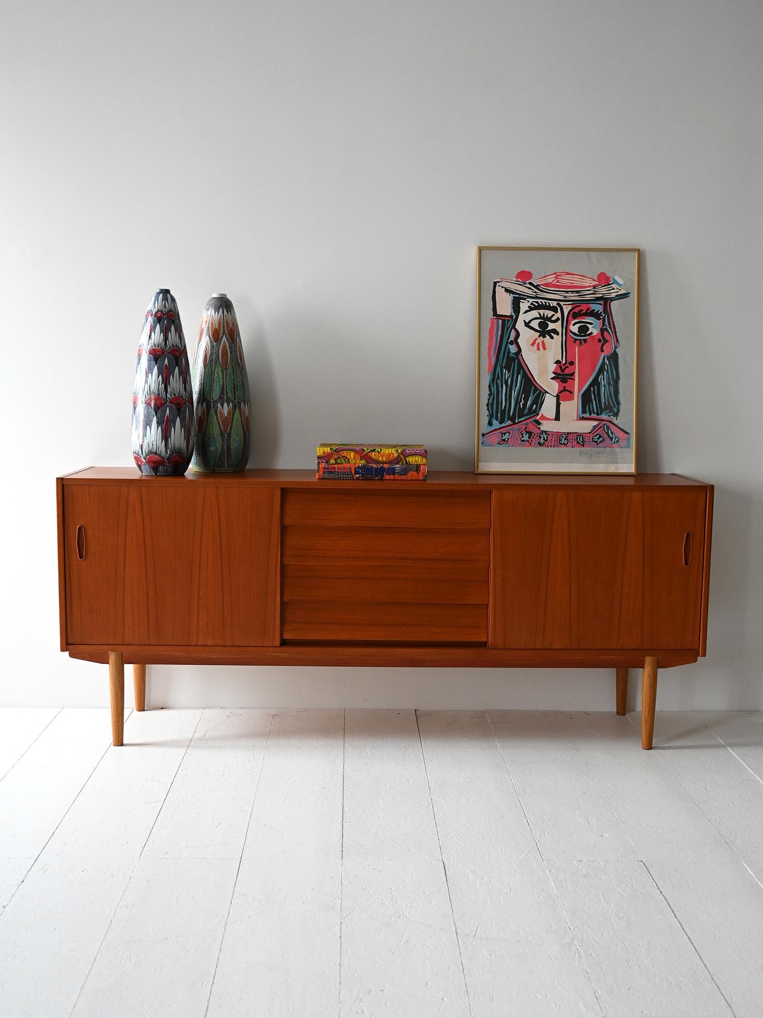 Teak sideboard with side sliding doors, center drawers and contrasting legs. Design by Nils Jonsson for Troeds.

Designed by Nils Jonsson for Troeds in the 1960s, this Scandinavian sideboard is made of teak with understated lines and harmonious