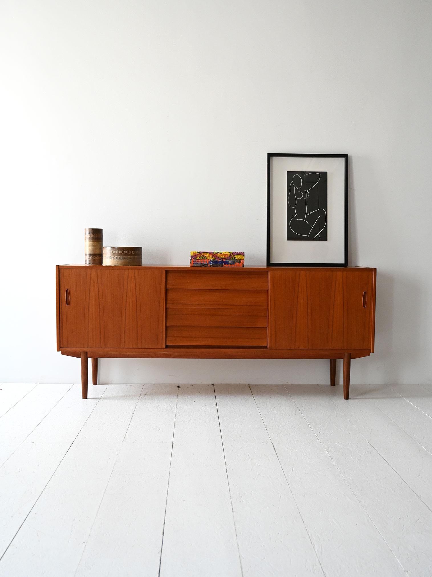 Sideboard in teak con ante scorrevoli laterali, cassetti centrali e gambe a contrasto. Design di Nils Jonsson per Troeds.

Disegnato da Nils Jonsson per Troeds negli anni '60, questo sideboard scandinavo è realizzato in teak con linee sobrie e