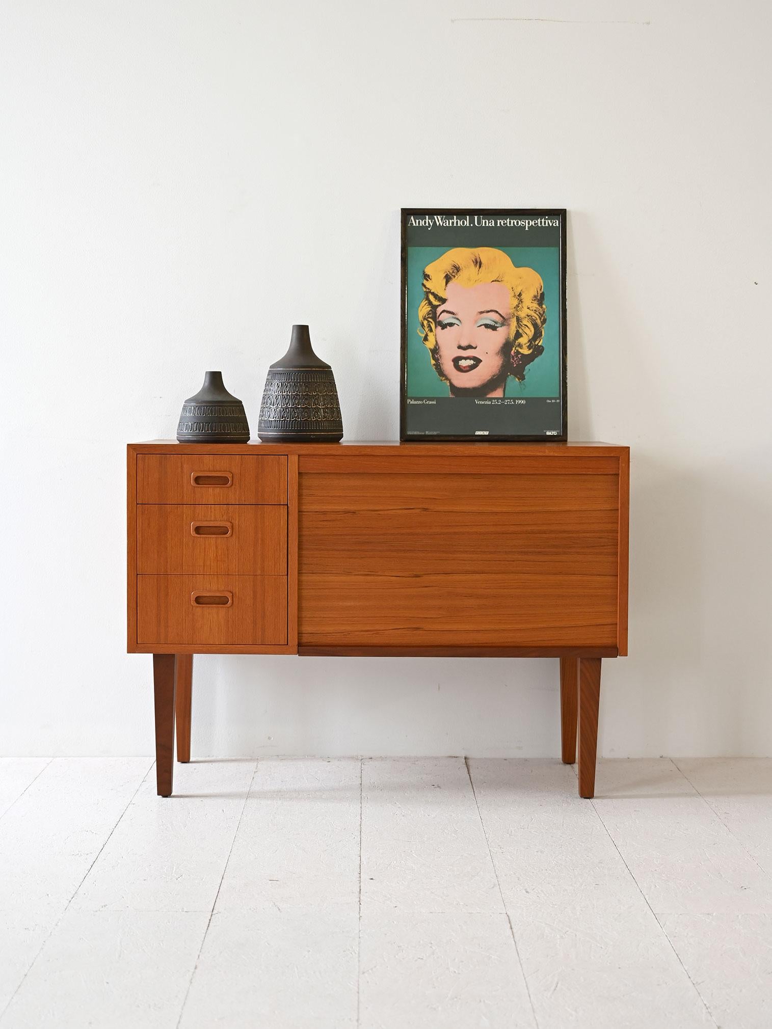 Scandinavian modernist cabinet with three drawers and storage compartment with shutter door that turns it into a small desk. 

The teak frame, linear design and refined details make it a sideboard suitable for different styles and environments.