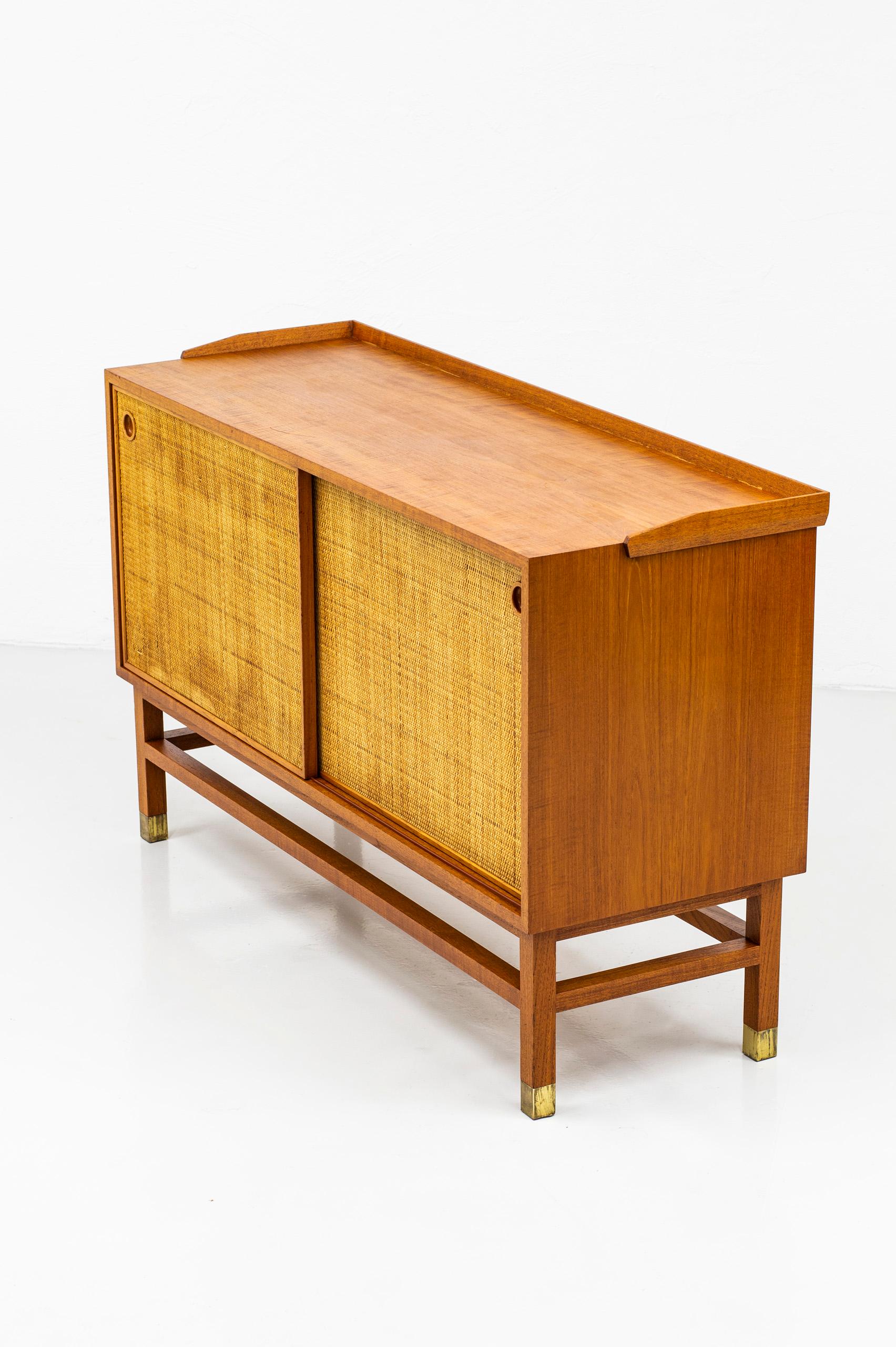 Sideboard produced in Sweden during the 1950s. Made from teak with contrasting rattan doors, ash wood on the inside and brass details on the legs. Adjustable and optional shelves on the inside. Very nice quality with teak veneer on the backside