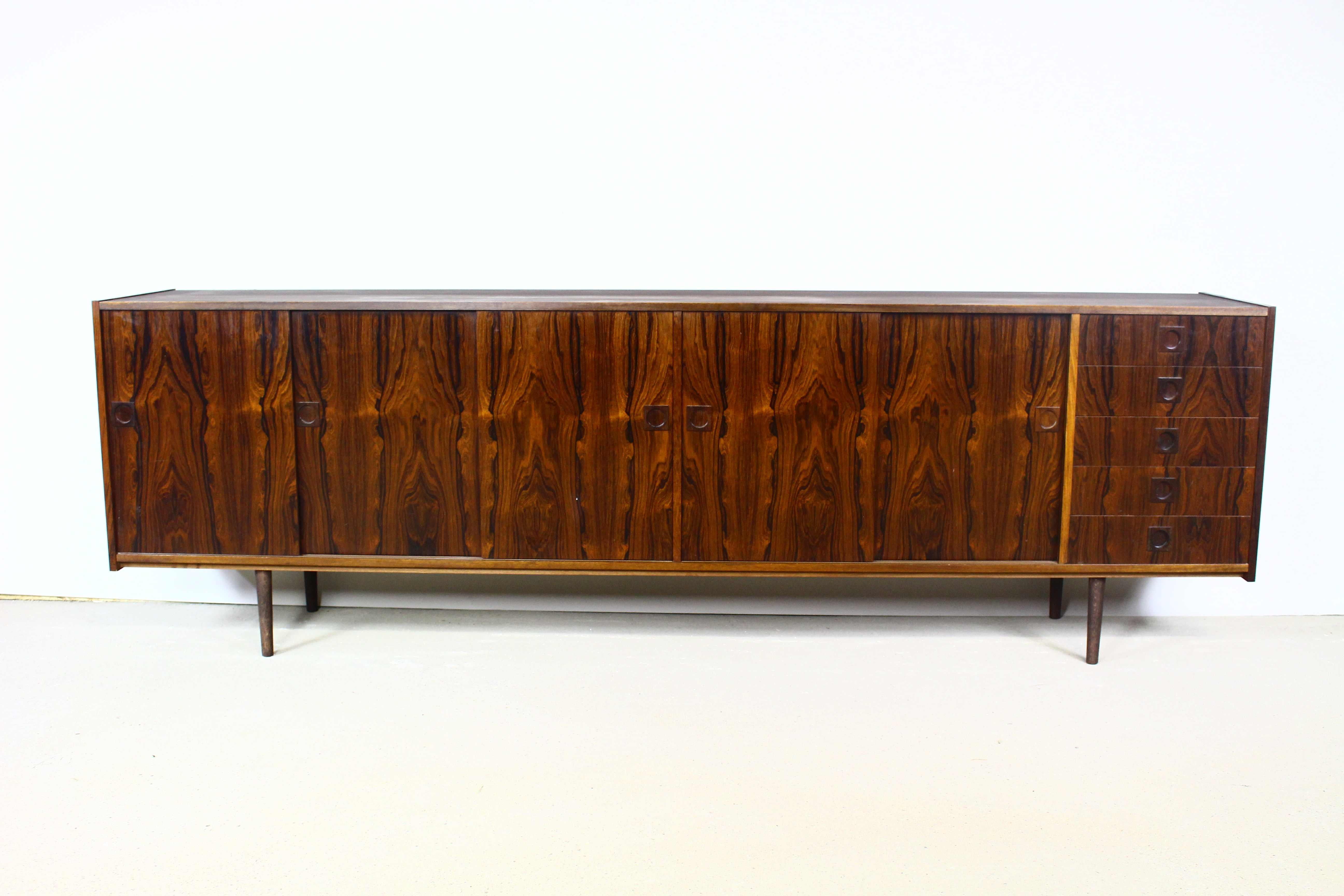 Danish rosewood sideboard from the 1960s.
The sideboard consists of five sliding doors, inside there are shelves, on the right there are five drawers.
The sideboard has contoured solid handles and beautiful graining.
Height adjustable shelves.

Top