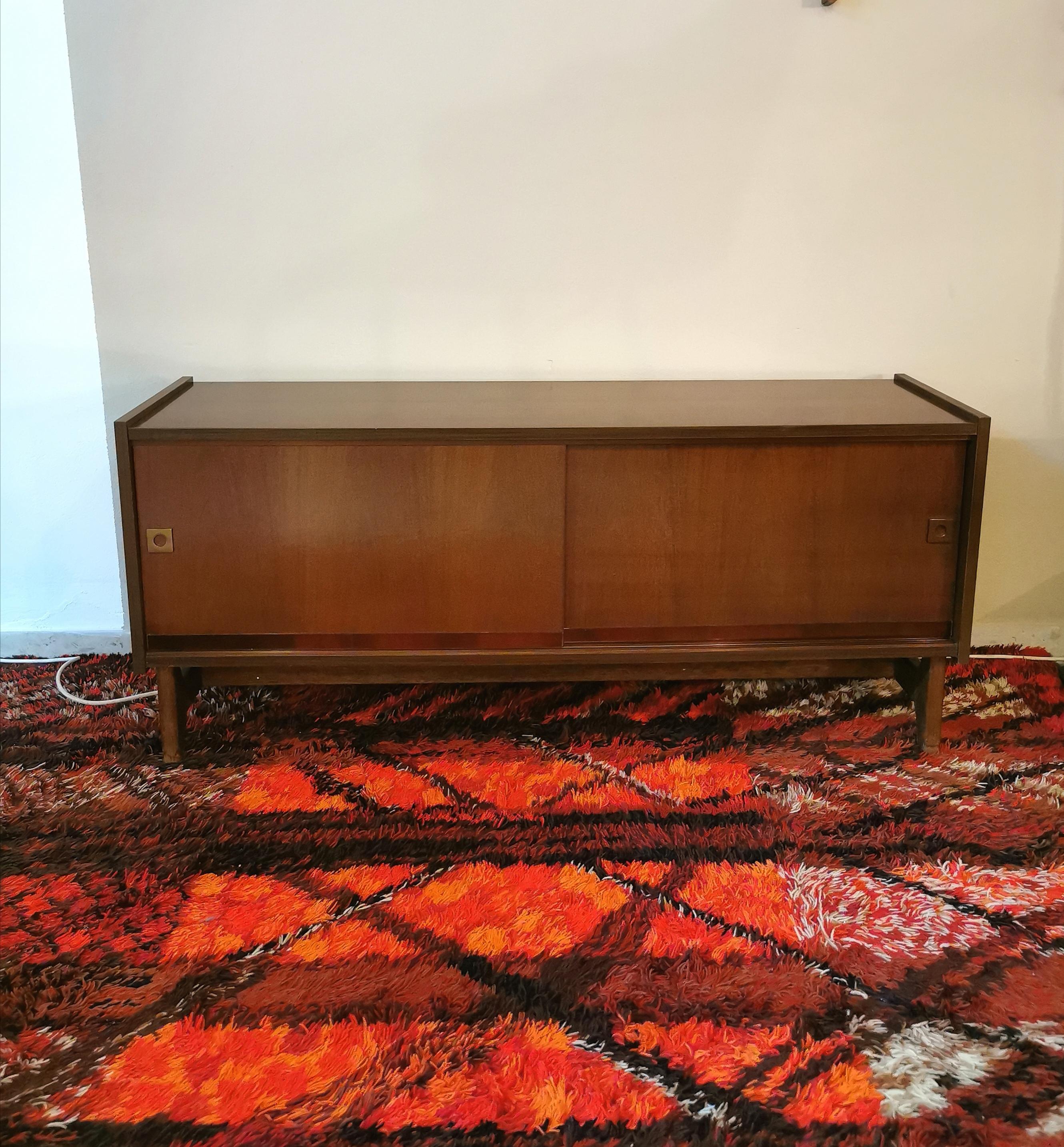 Sideboard in walnut wood by the unknown designer with 2 sliding doors with small brass handles, where inside there are 2 rectangular glass shelves. Made in Italy in the 70s.

