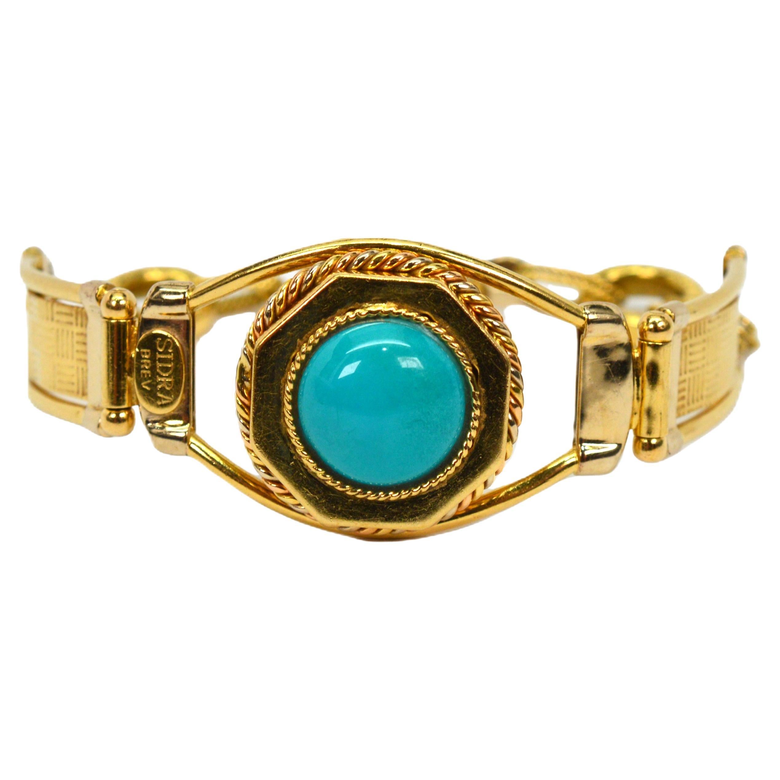 Enjoy this 18 karat yellow gold transitional style link bracelet that boldly features a colorful round Turquoise Cabochon. The 
13.5 mm stone is mounted in a raised hexagon-shaped bezel of 18 karat gold that beautifully highlights it as a focal