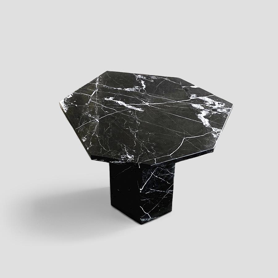 Siebeneck es una mesa auxiliar que parte de la pureza formal para resaltar la materialidad del mármol negro. Su parte superior heptagonal -de líneas precisas y bordes definidos- descansa sobre una sólida base del mismo material, creando una pieza