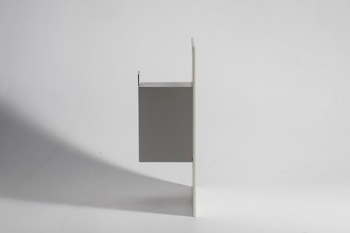 Une composition artisanale sculptée dans le bois, élégamment revêtue de blanc. Dans sa forme, une peinture noire audacieuse se répand organiquement, juxtaposée à une écriture à main levée qui insuffle mouvement et spontanéité à l'œuvre. Une petite