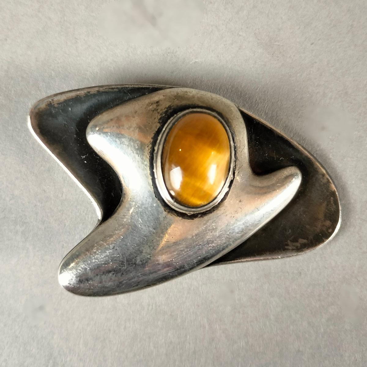 A modernist 1970's Taxco, México Sterling Silver with Niello finish and a tiger's eye cabuchon brooch by Sigifredo Pineda. The curved 2-layer design is in clear silver finish in front and with niello on the back. The 15 x 11 mm tiger's eye oval