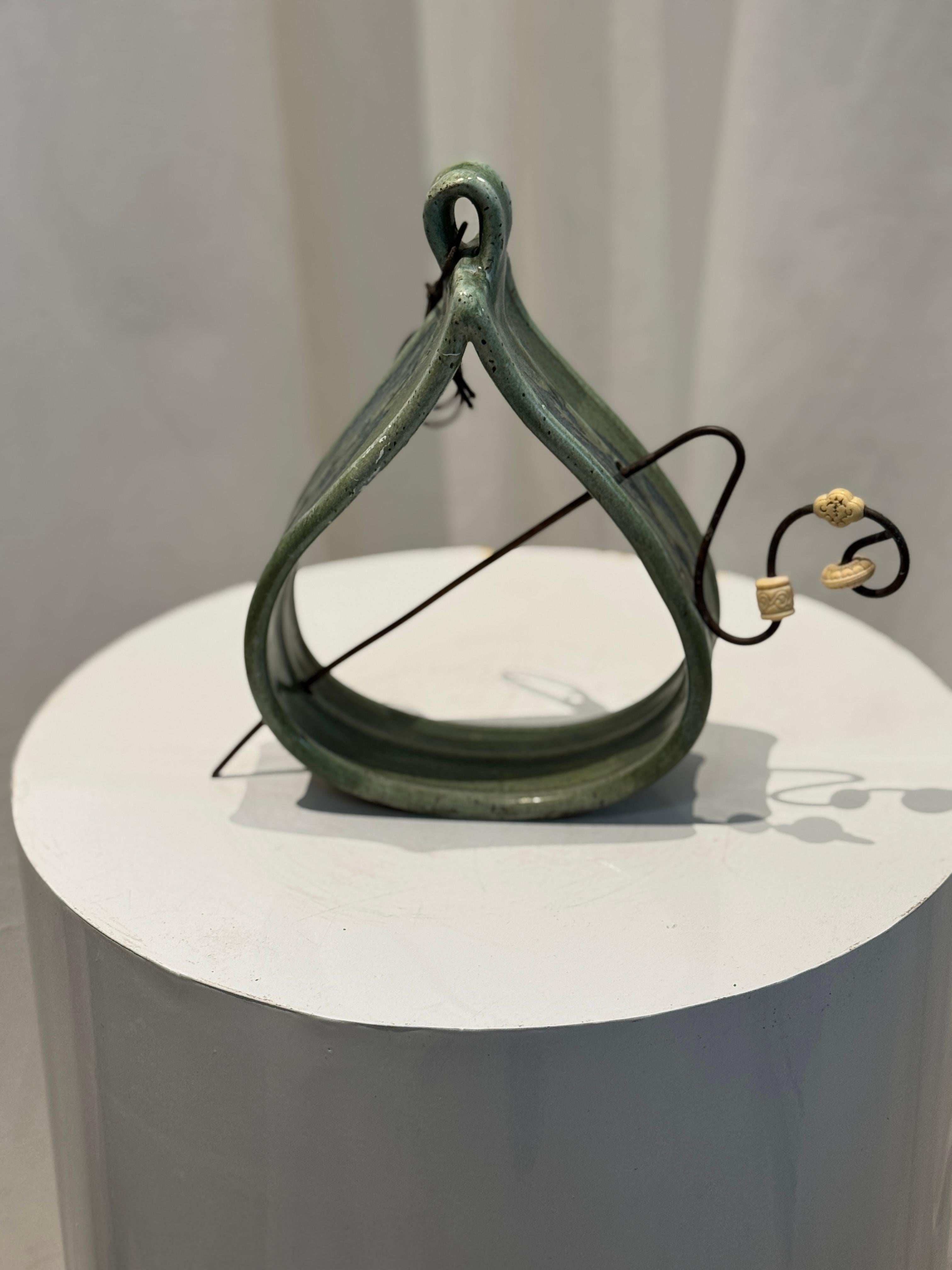 Esta Firma J.S. La Pieza Decorativa Colgante es una maceta de pared de cerámica bellamente elaborada con un rico esmalte verde y una elegante forma curvada. Con un lazo para colgar integrado y una robusta varilla de metal, esta pieza vintage única