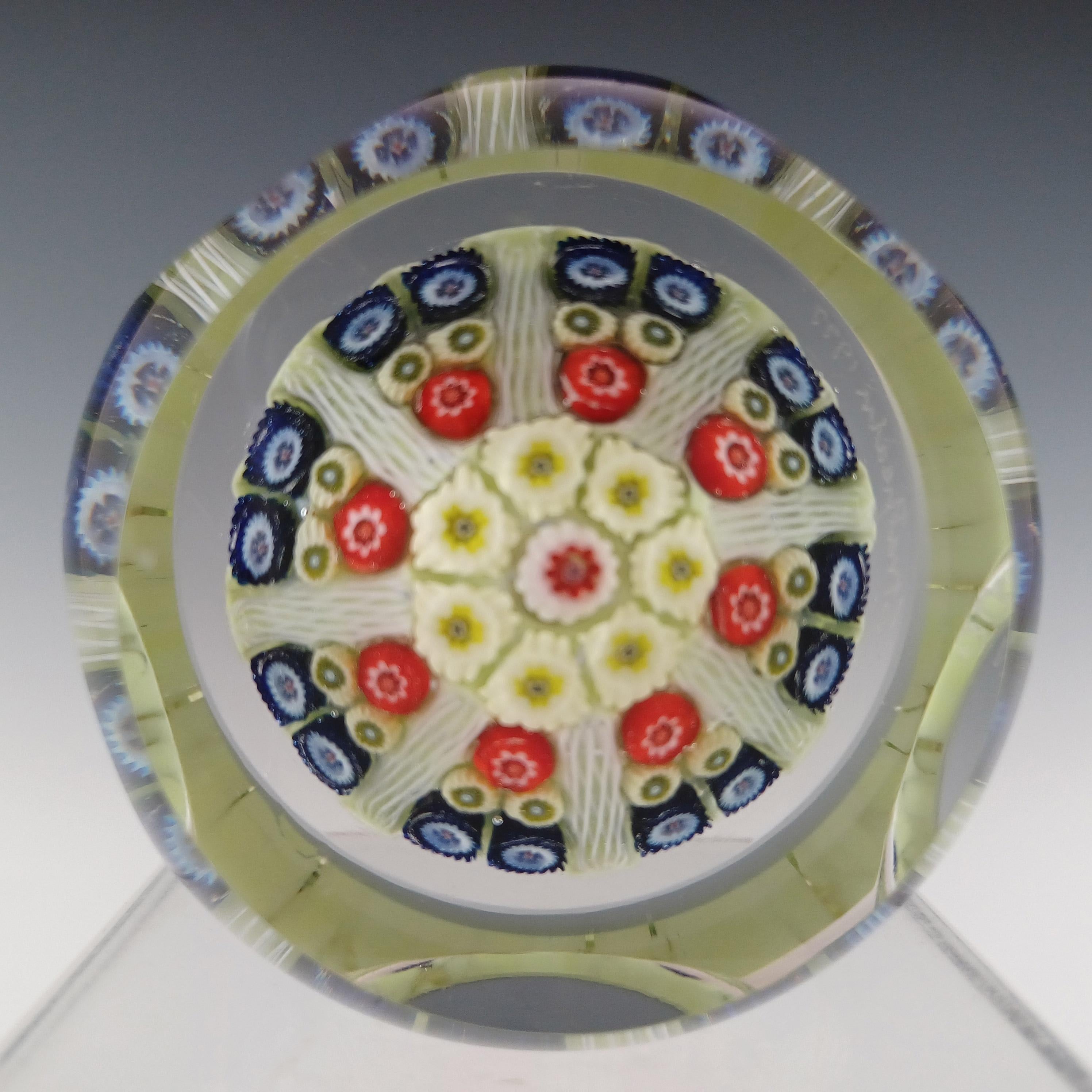 Pisapapeles de cristal escocés con bastones millefiori rojos, amarillos, azules y blancos, sobre una base de fondo amarillo, separados por una filigrana de celosía blanca de ocho 