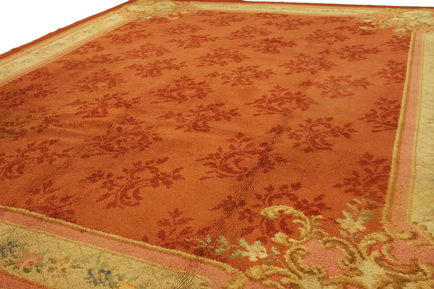 This is an antique European carpet woven in Holland circa 1900 and measures 380 x 310CM in size. this rug has a simplistic yet elegant field design that incorporates repeating shrub motifs in a slightly darker red hue compared to the softer red