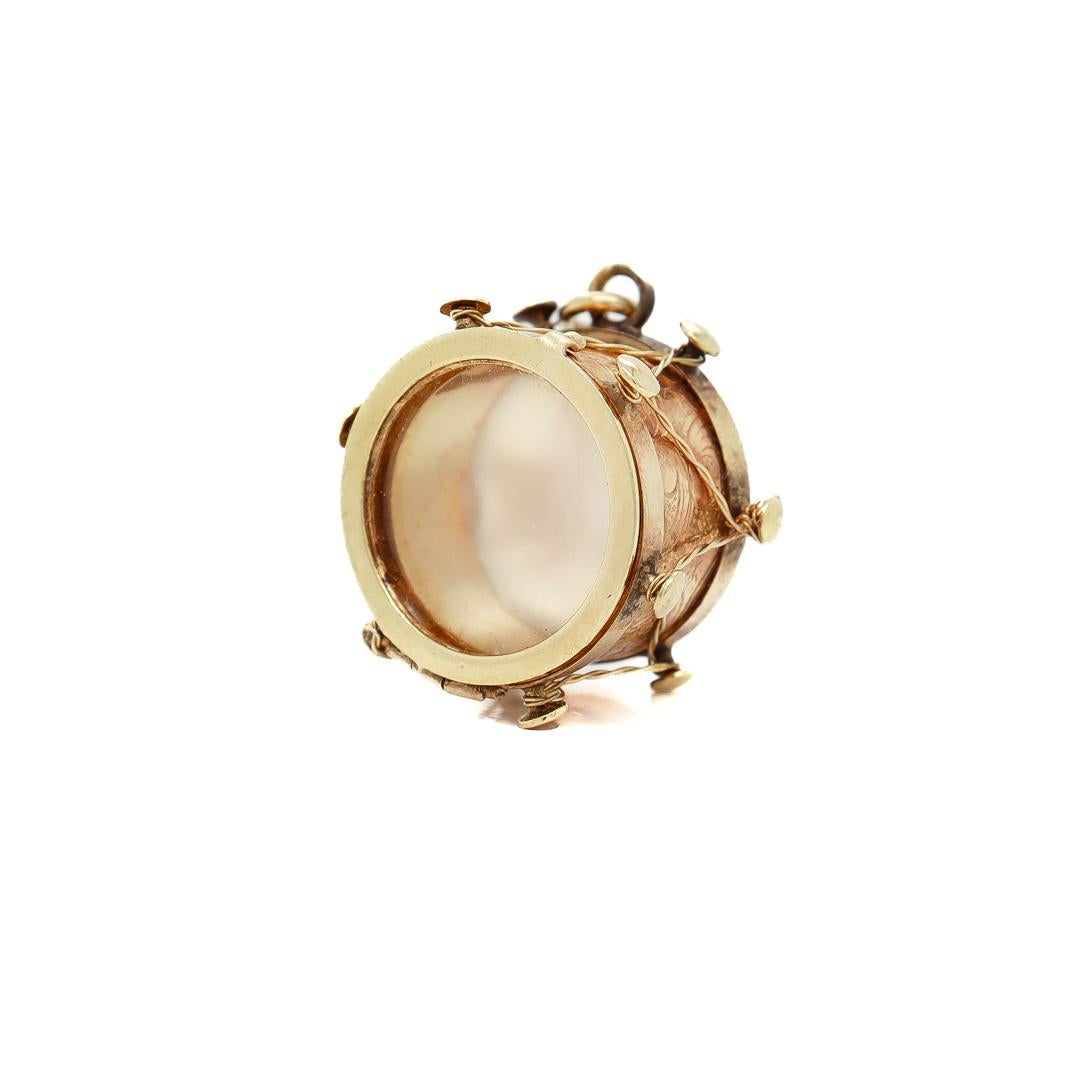 A fine Mid-Century signed figural charm for a bracelet.

In 14k gold.

By the JM Fisher Company of Attleboro, Massachusetts.

In the form of a drum with mother-of-pearl base and hinged lid top that opens to reveal the interior and with twisted gold