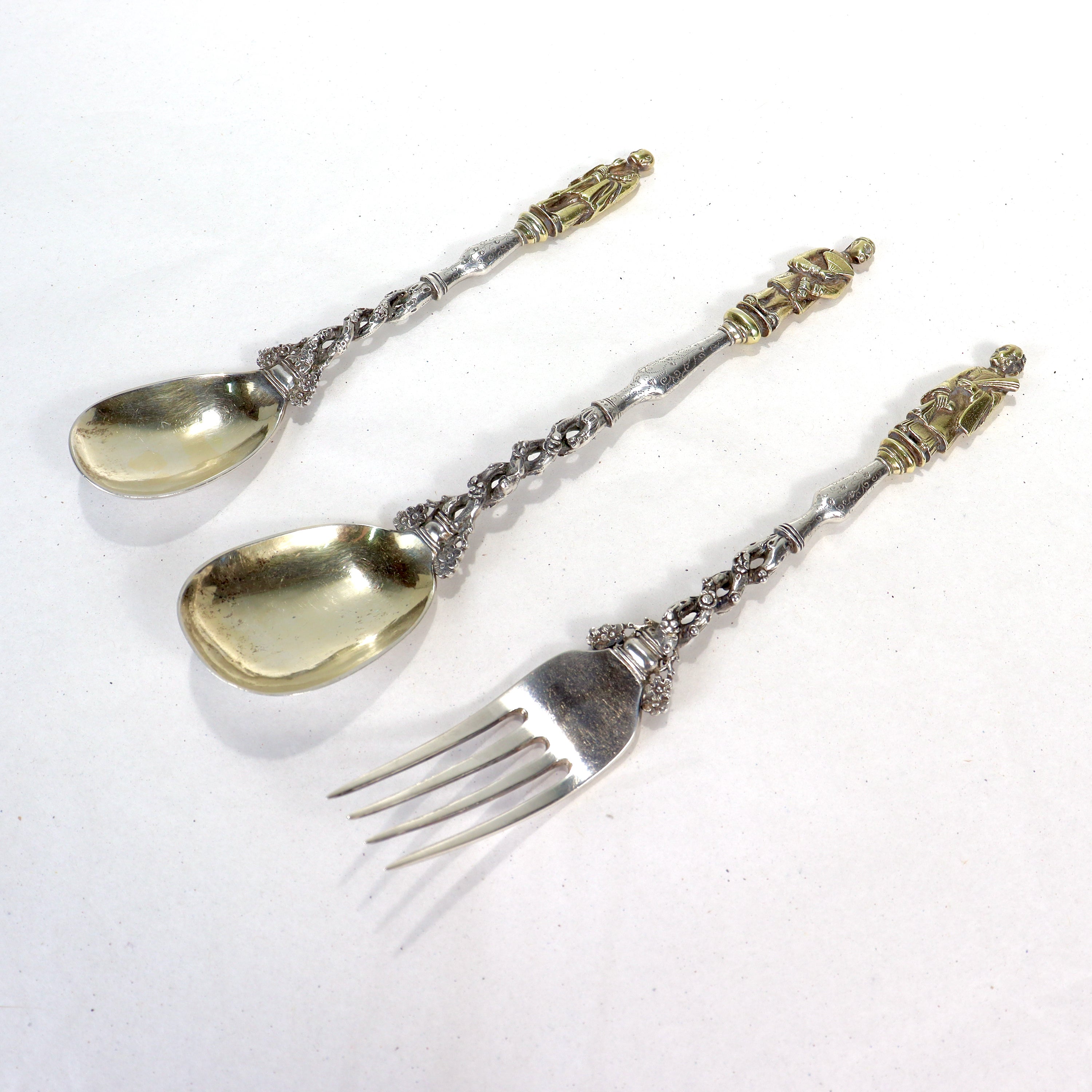 A fine set of antique Chinese export silver flatware.

Consisting of two (differently sized) spoons and a dinner fork.

The tops of the handles terminate in full figural Chinese figures and are finished with a gold wash. Each finial has a different