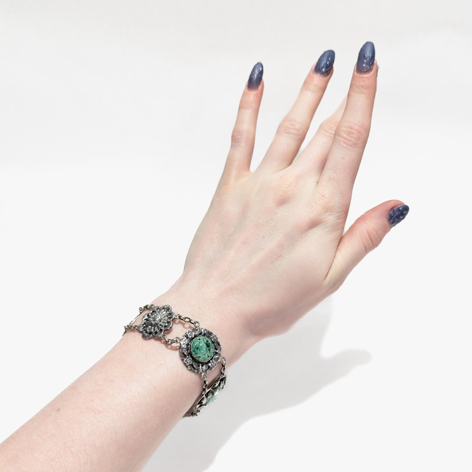 Un raffinato bracciale cinese firmato.

Composto da 6 medaglioni d'argento collegati da maglie ovali a catena. 

Quattro medaglioni hanno piccole placche di giada intagliata.

Sul retro sono riportati i caratteri.

Un gioiello cinese semplicemente