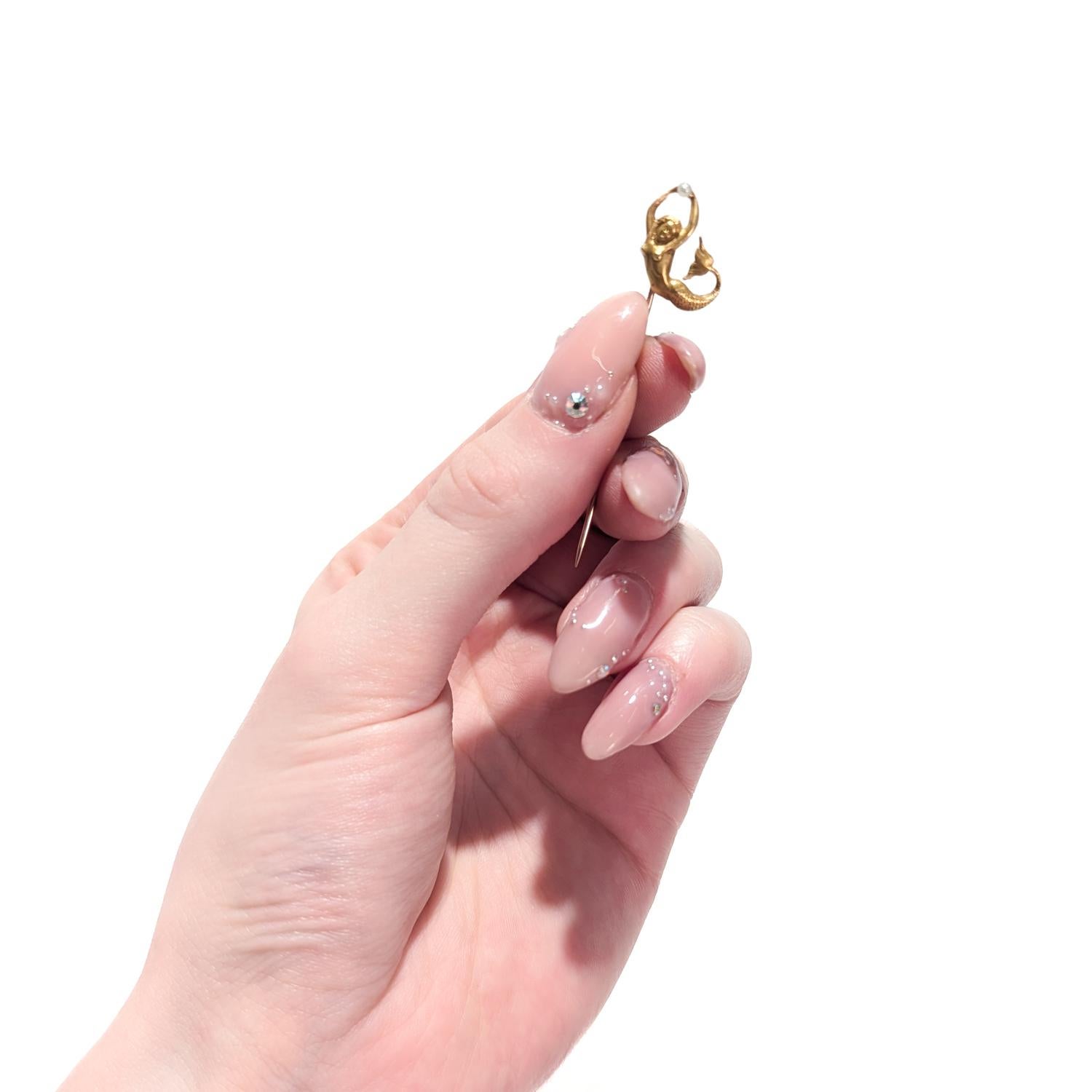A fine signed vintage gold & pearl stickpin.

In 10 karat yellow gold.

In the form of a finely modeled mermaid holding a pearl.

Her hands are held aloft and she grasps a pearl between them.

Marked to the pin stem B&N / 10K

Simply a wonderful
