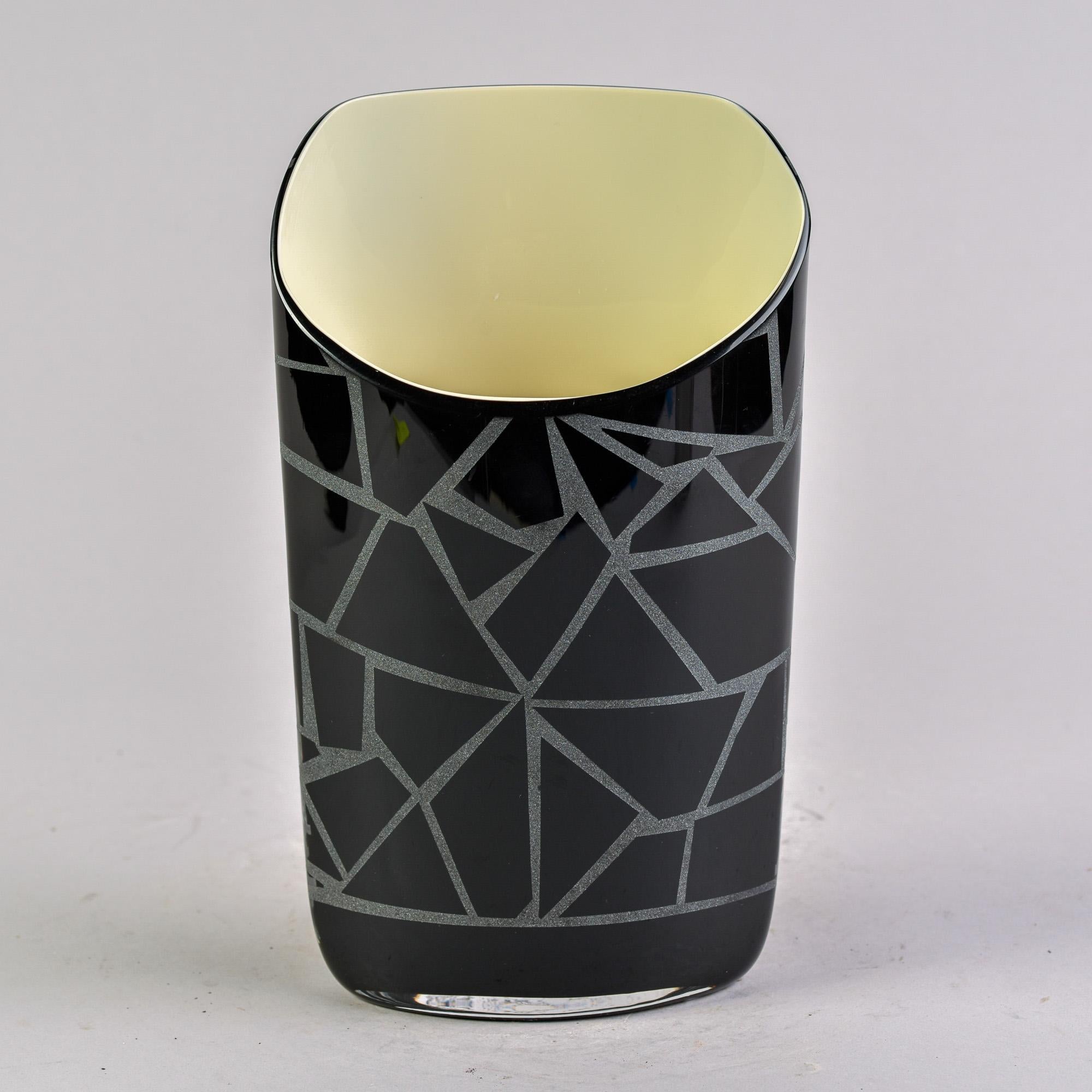 Found in Italy, this Carlo Moretti Murano glass vase dates from the 1980s. The exterior is composed of black glass with an abstract design etched on the surface. Interior is  cream color glass and the vase has an uneven rim with the back taller than