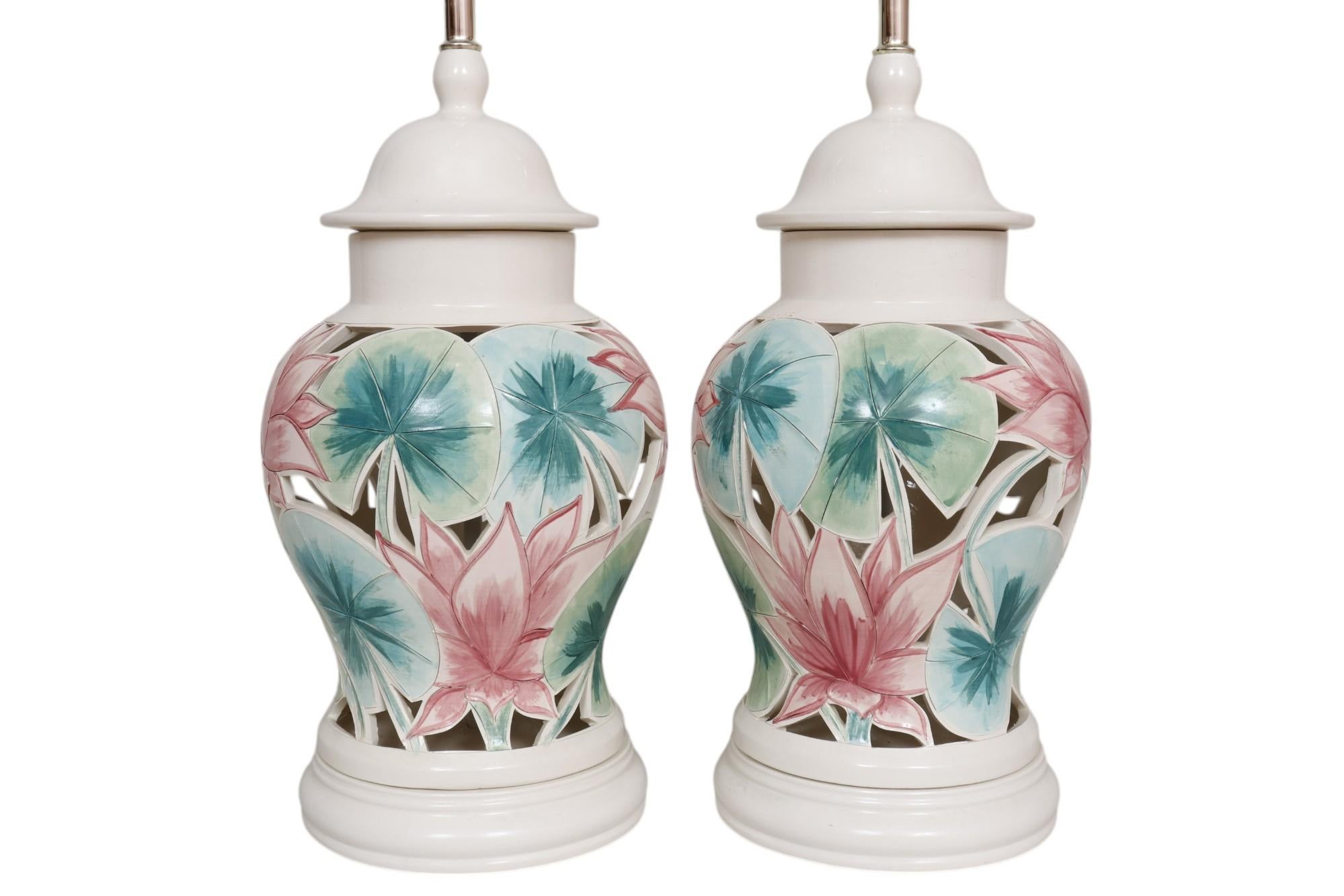A pair of floral ceramic ginger jar table lamps, signed “Sally ‘95”. White vases are hand painted with lotus leaves and flowers in green and pink. Pierced with cut outs around incised foliage to give depth to the lamp bodies, finished with beveled