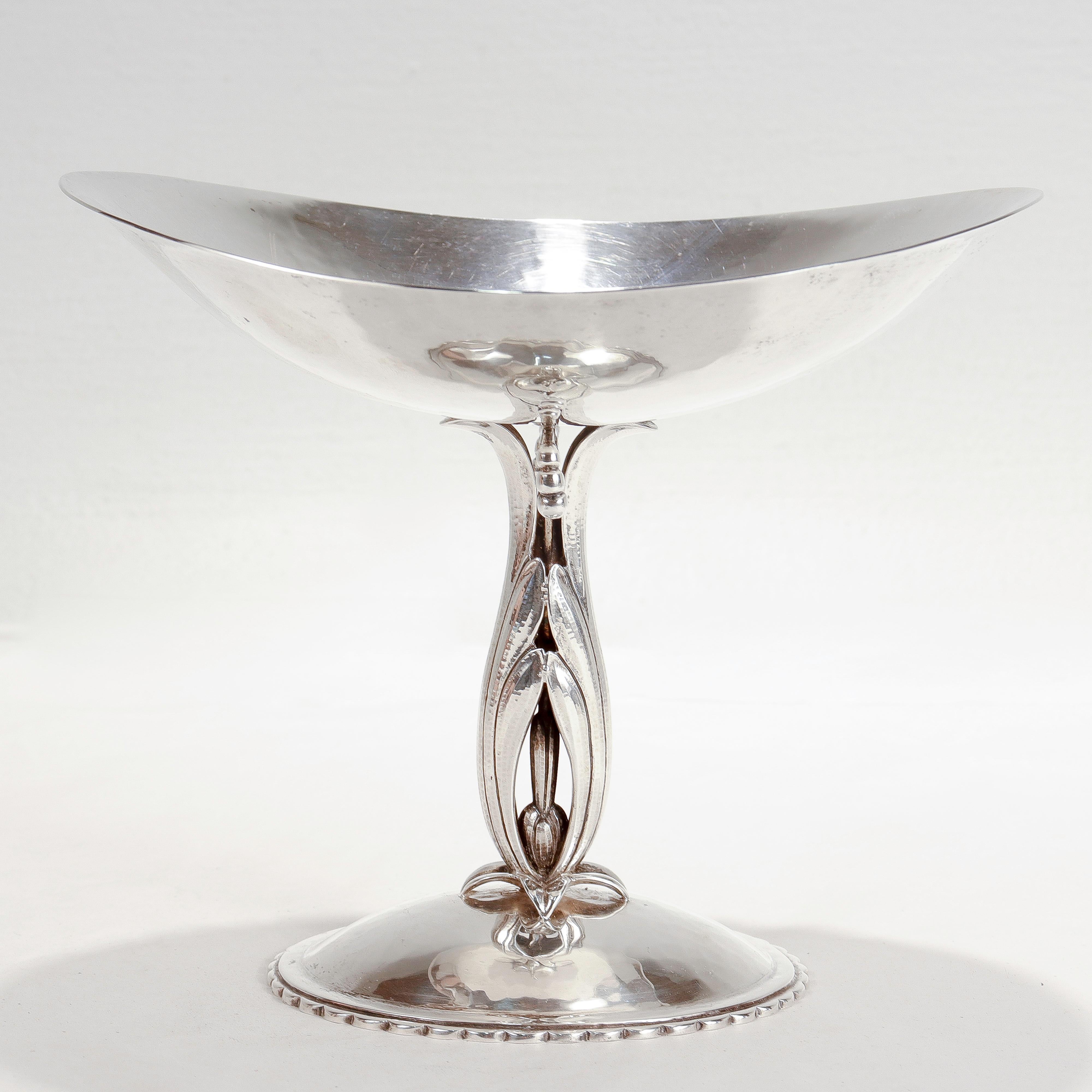 A fine American Arts & Crafts tazza or footed compote.

In sterling silver.

By Cellini Craft of Chicago.

With a stylized floral & foliate pedestal, an oval hand-hammered bowl, and a convex scalloped base.

Simply a wonderful piece by Cellini