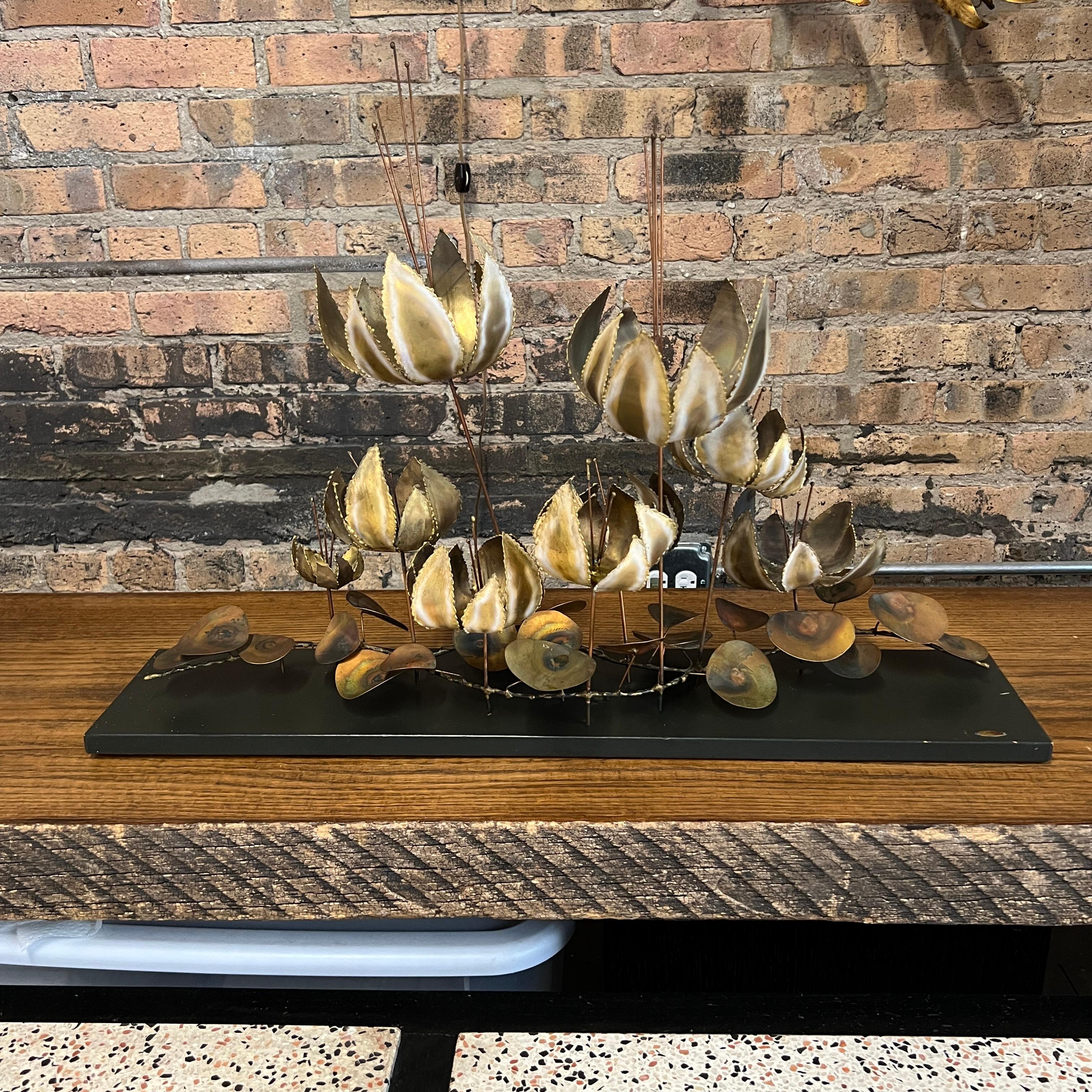 This is a lovely floral brutalist table sculpture by C. Jere dated 1967.  It sits on a ebonized wood board.  It is impressive in size.

There are some imperfections to the base (see closeup images) and a few very light scratches to the metal (see