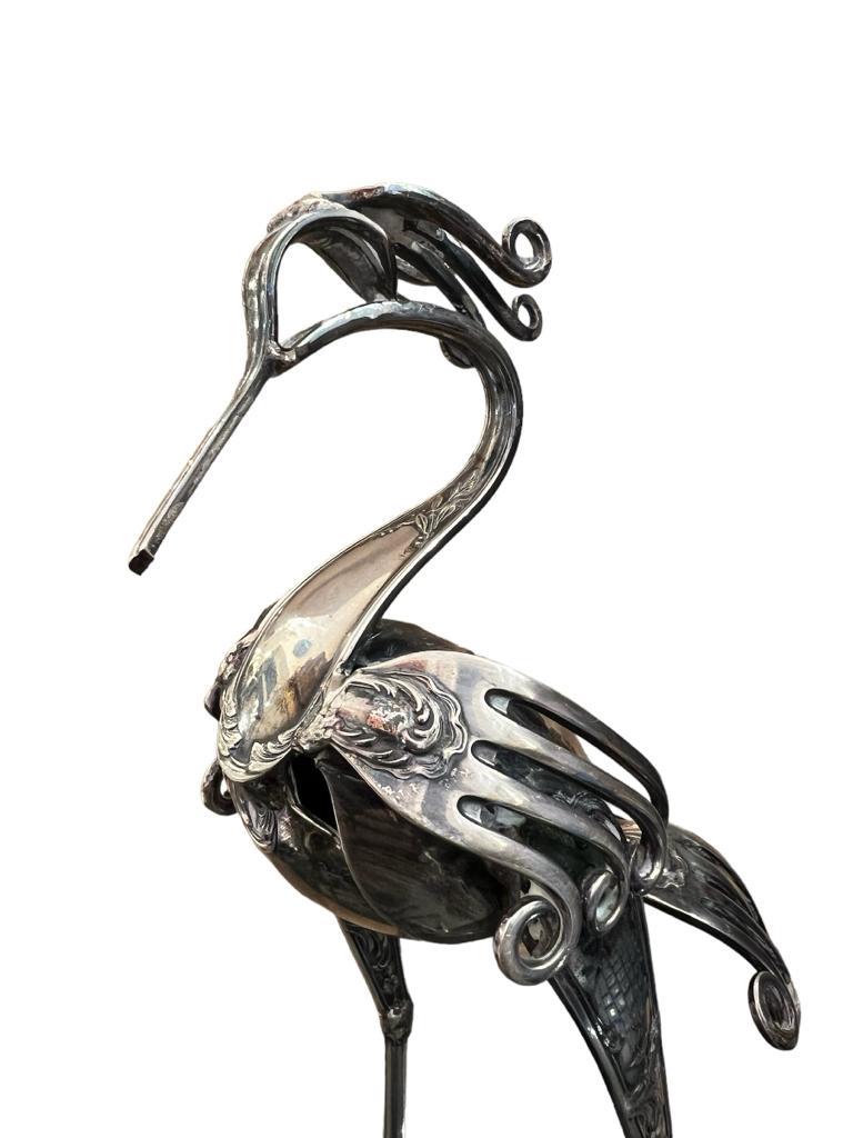 This unique cutlery sculpture, crafted by the French artist Gérard Bouvier who was born in 1942, is a mid-century masterpiece representing a heron bird intricately fashioned from silver-plated antique forks, knives, and spoons. The sculpture bears