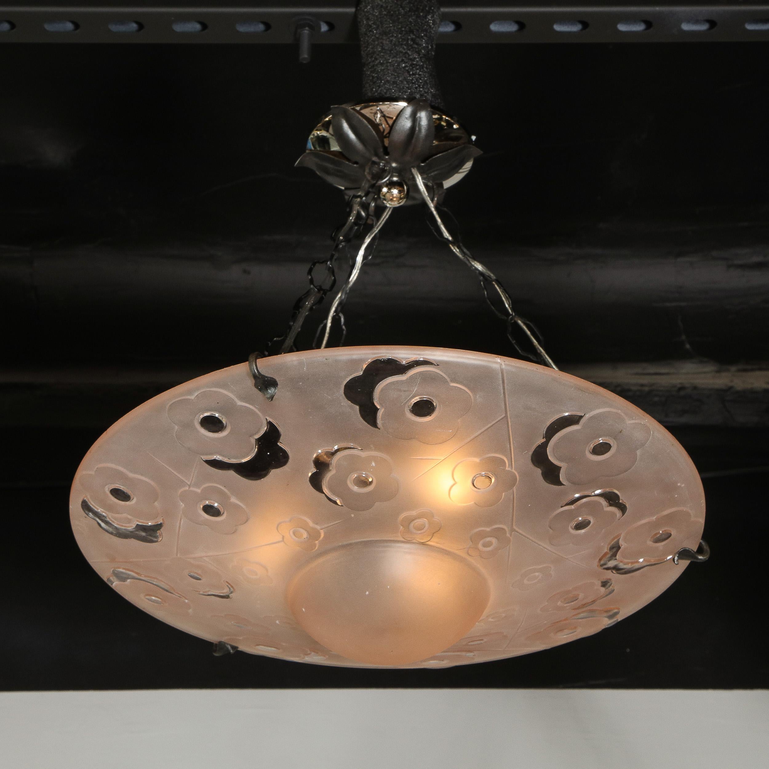 This stunning signed Degué Art Deco chandelier was realized in France circa 1930. It features a circular slighly convex body with a domed body in frosted rose colored glass with cubist floral motifs (resembling stylized cherry blossoms) etched in