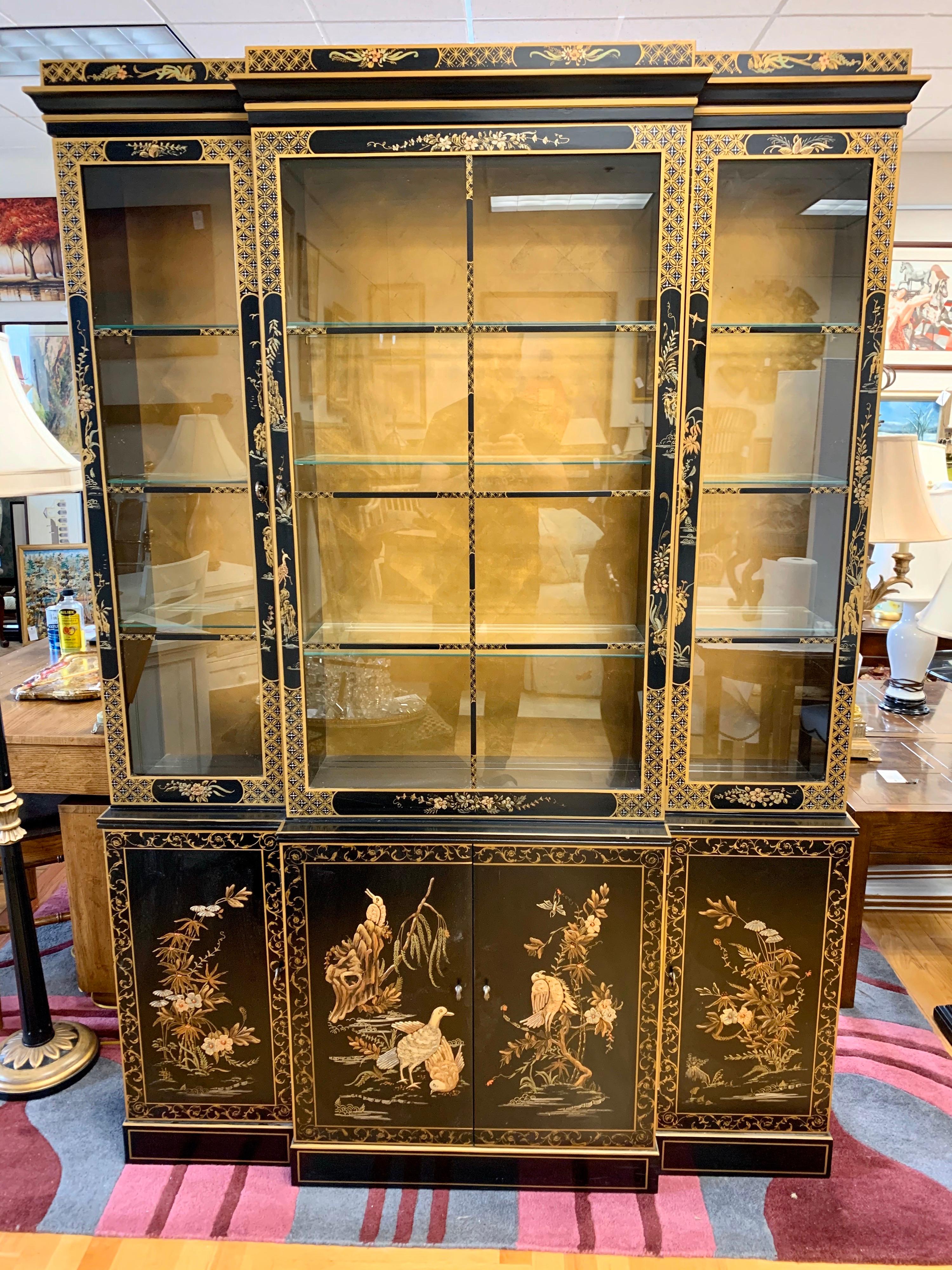 Elegant midcentury chinoiserie japanned one-piece china cabinet features beautiful hand painted motif and gold detail on the front and sides. Three top front doors open to glass shelves which illuminate from above. Background is gold leaf. Bottom