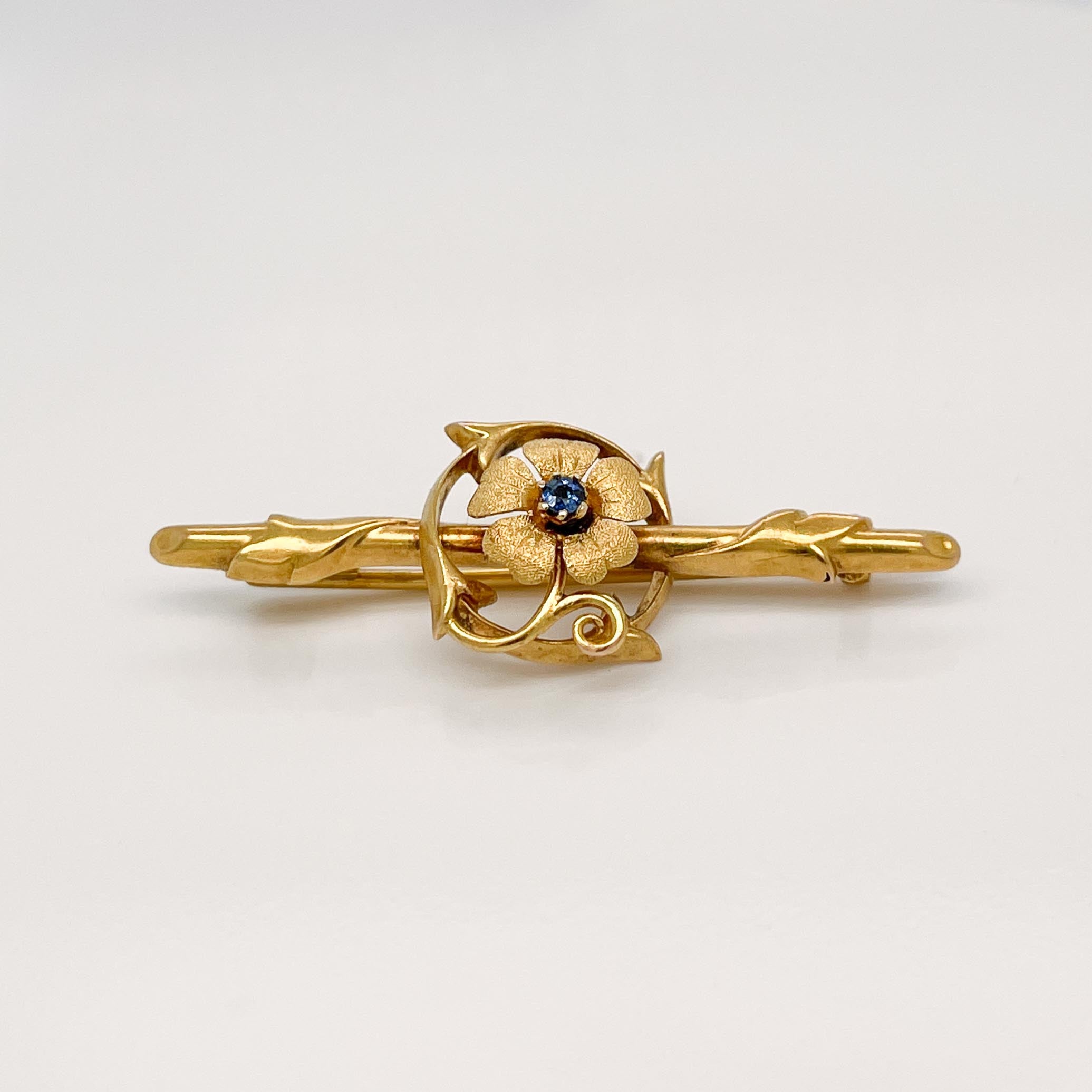 A fine antique Edwardian brooch.

In 15 karat yellow gold. 

In the form of a flower & vine set on a twig formed bar. The flower is set with a small round cut sapphire gemstone. 

Marked to the reverse for the maker F.B. and with English gold